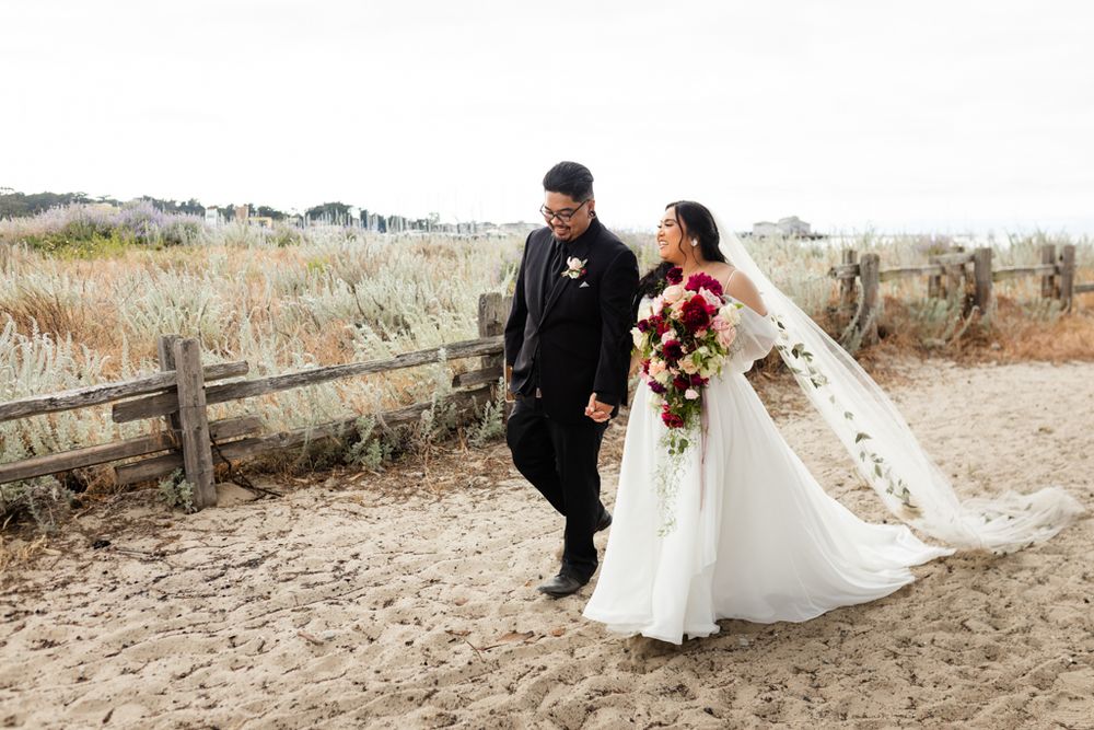 A couple walks along a rustic coastal path on their wedding day with dramatic scenery.