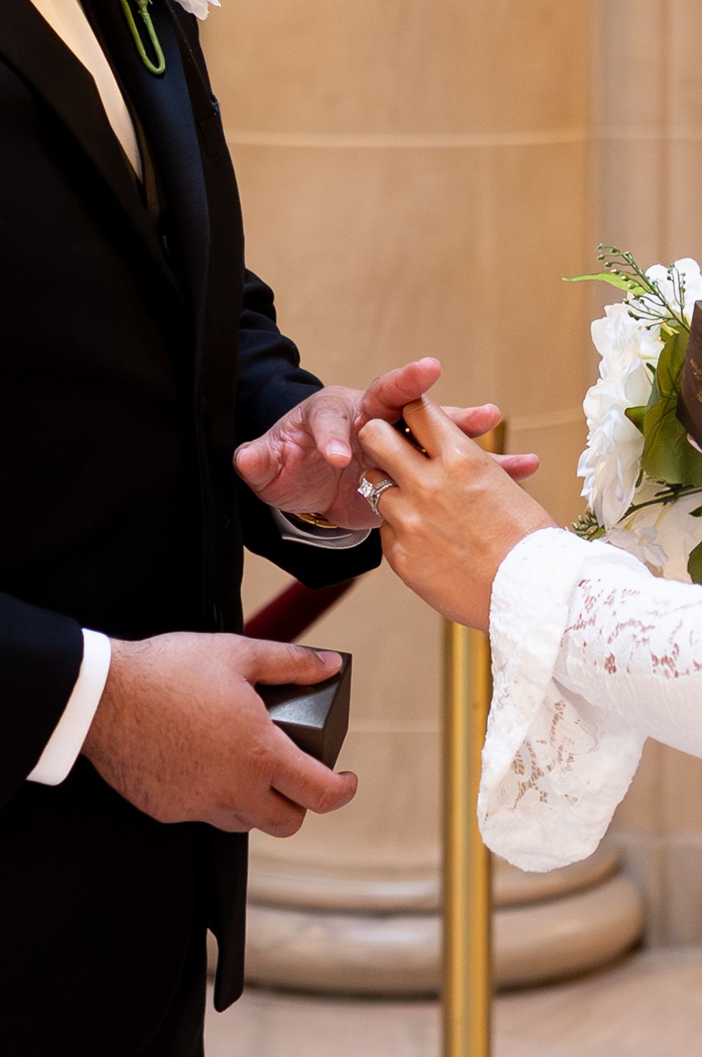 Bride placing wedding ring on groom's finger during ceremony, holding bouquet of white flowers.