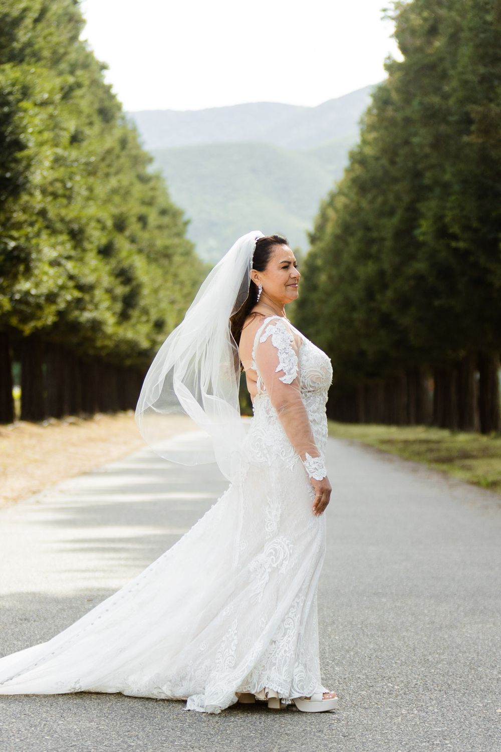 A bridal portrait on a tree-lined road with mountains in the background.