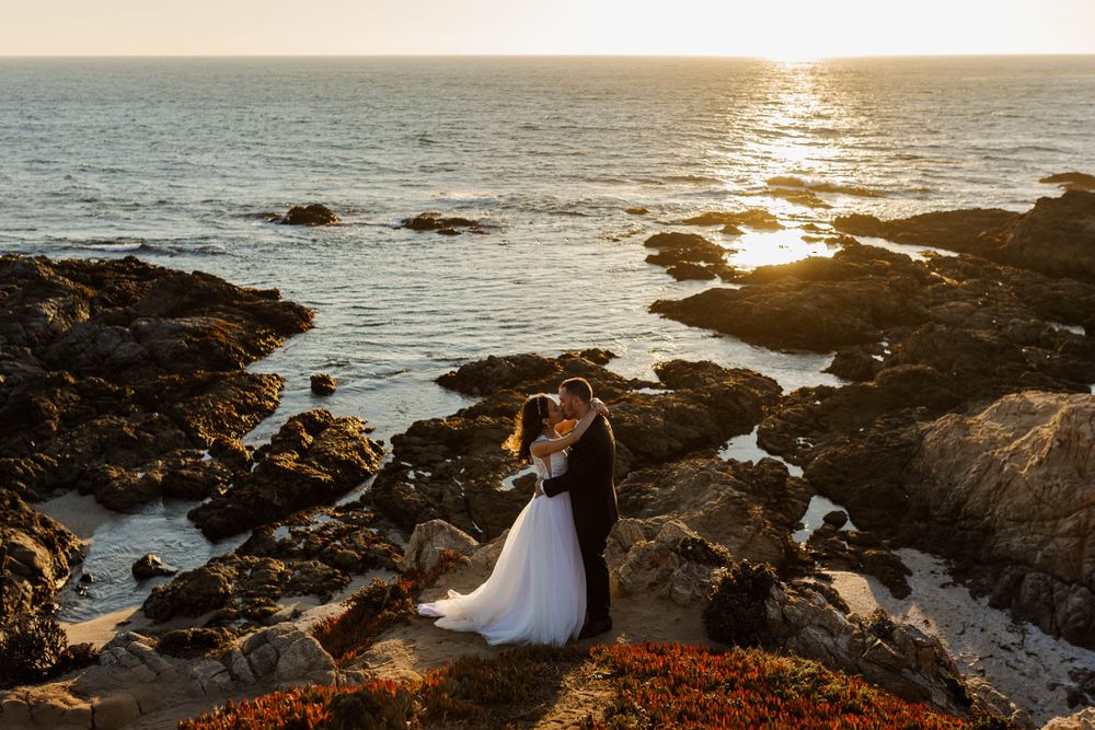 A sunset wedding photo on rocky coastal cliffs with golden light reflecting on the ocean.