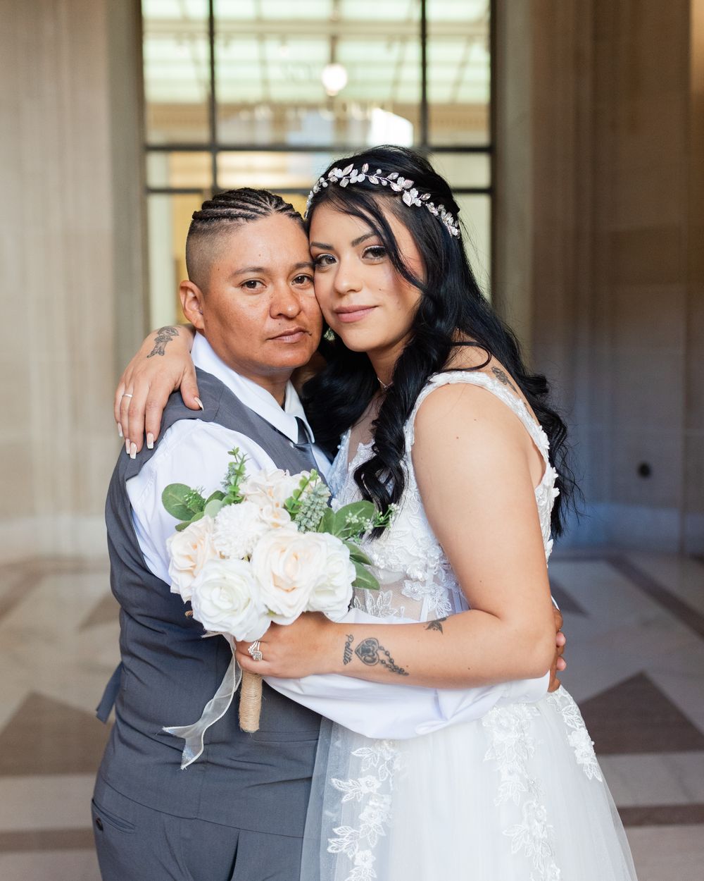A happy couple embraces while holding a bouquet of white roses on their wedding day.