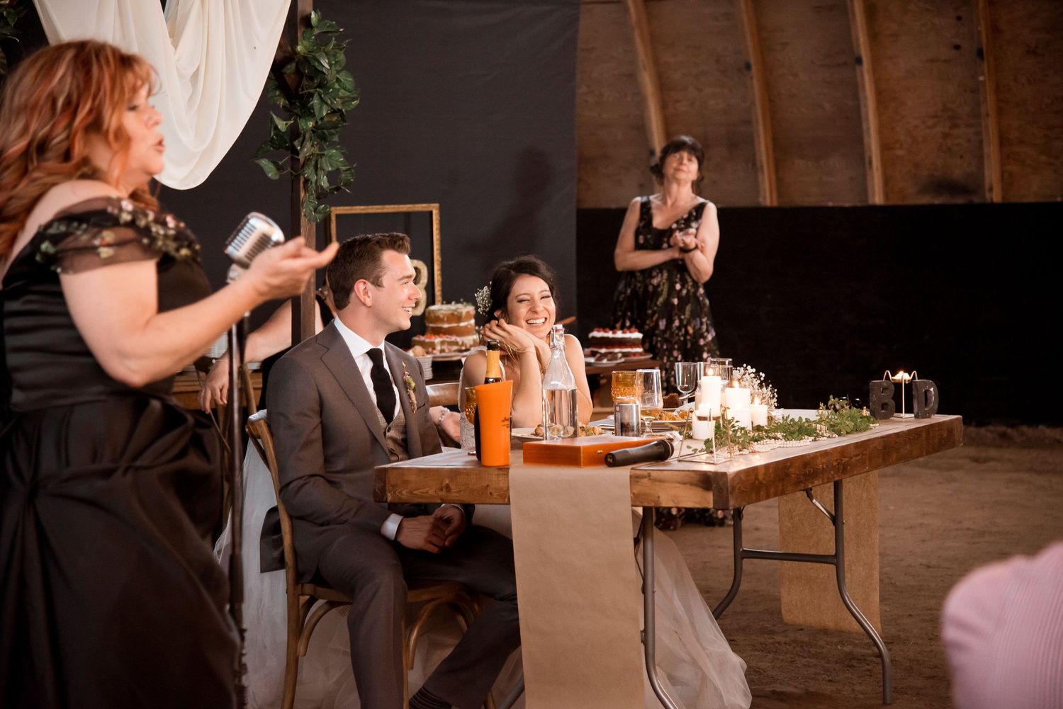Wedding reception guests listening to a heartfelt speech at a candlelit rustic barn venue during an evening celebration.