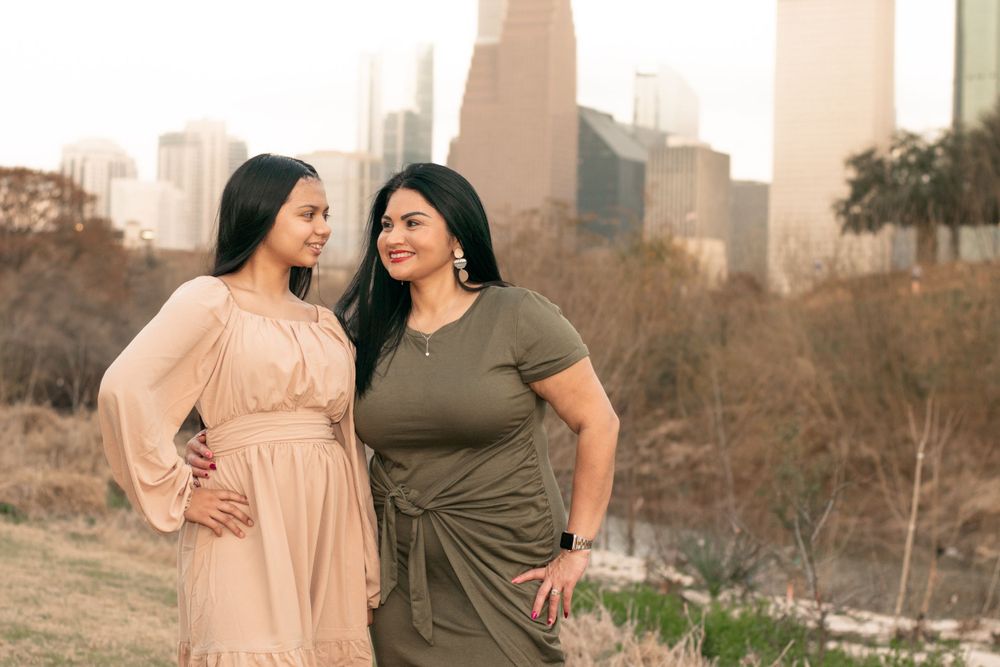 Two women in casual dresses smile and pose together with urban skyline in the background.