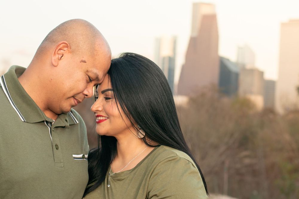 A romantic couple shares an intimate moment against a backdrop of downtown city buildings at sunset.