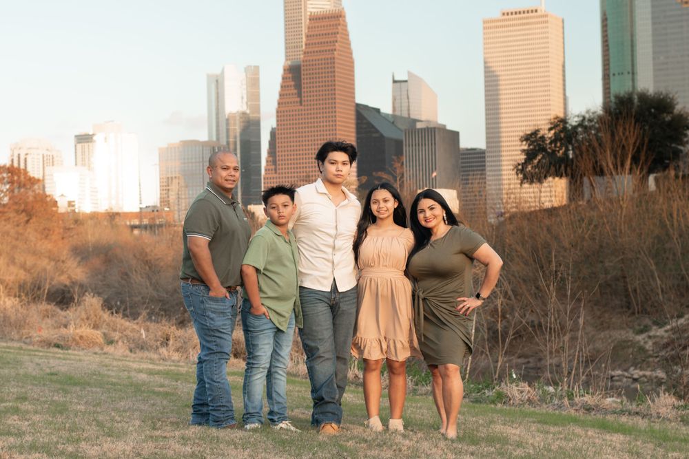 Family portrait outdoors with Houston city skyline in warm sunset lighting.