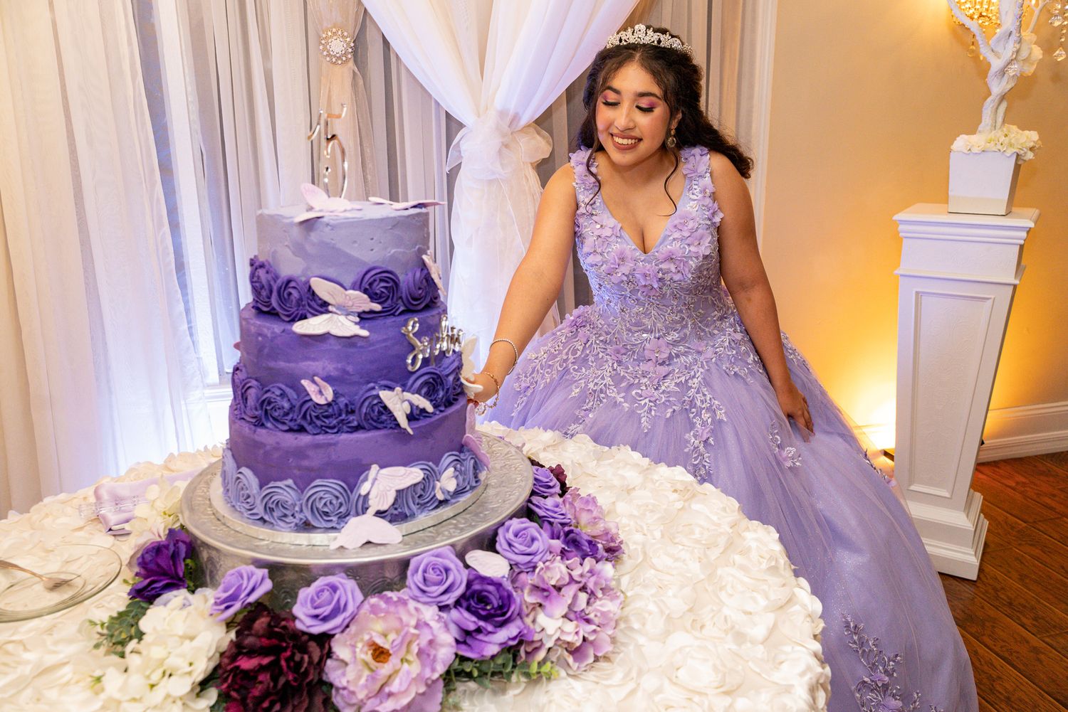 A stunning purple quinceanera celebration featuring an elegant tiered cake decorated with butterflies and matching floral arrangements.