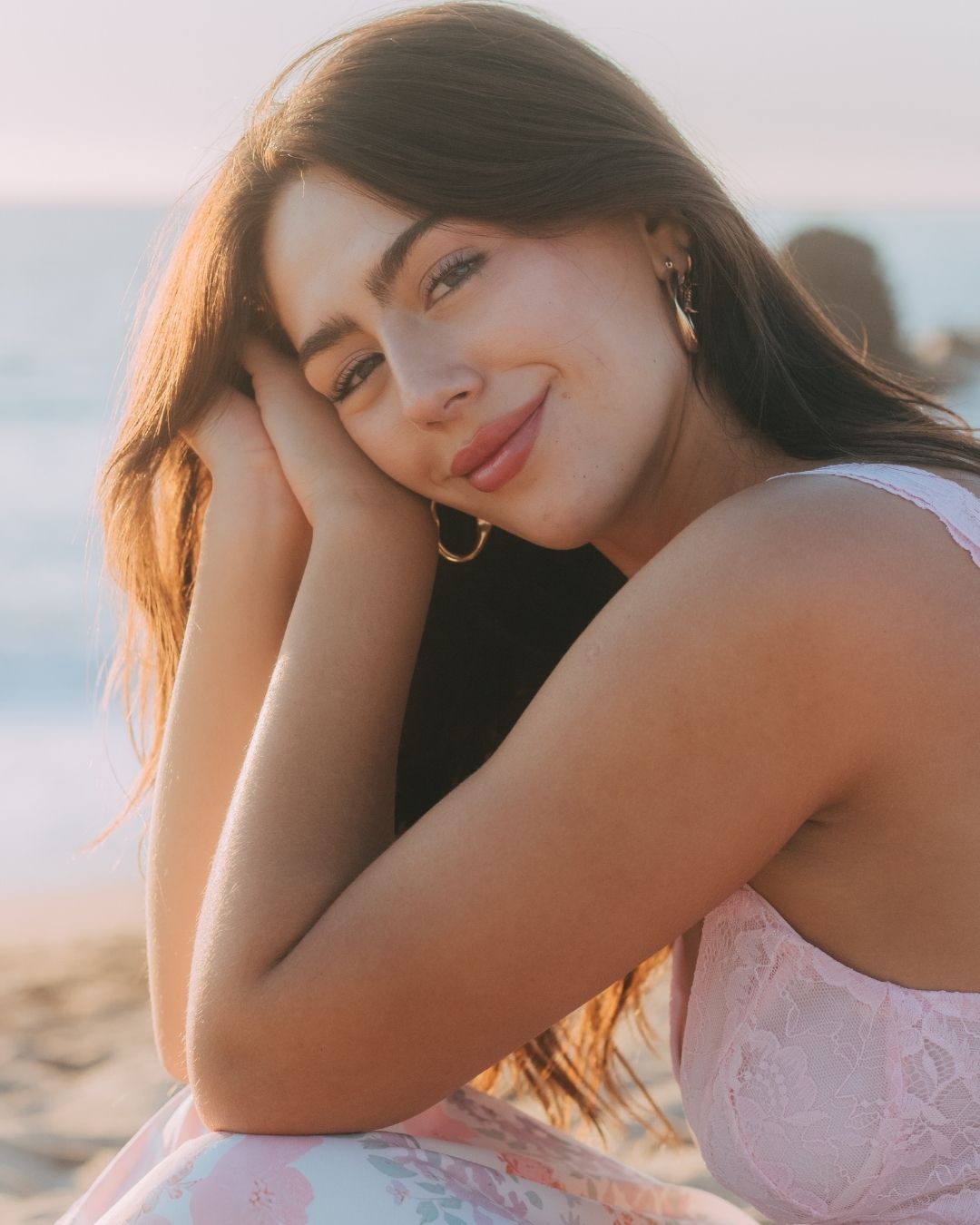 Beautiful brunette woman smiling softly at sunset beach with golden hoop earrings.