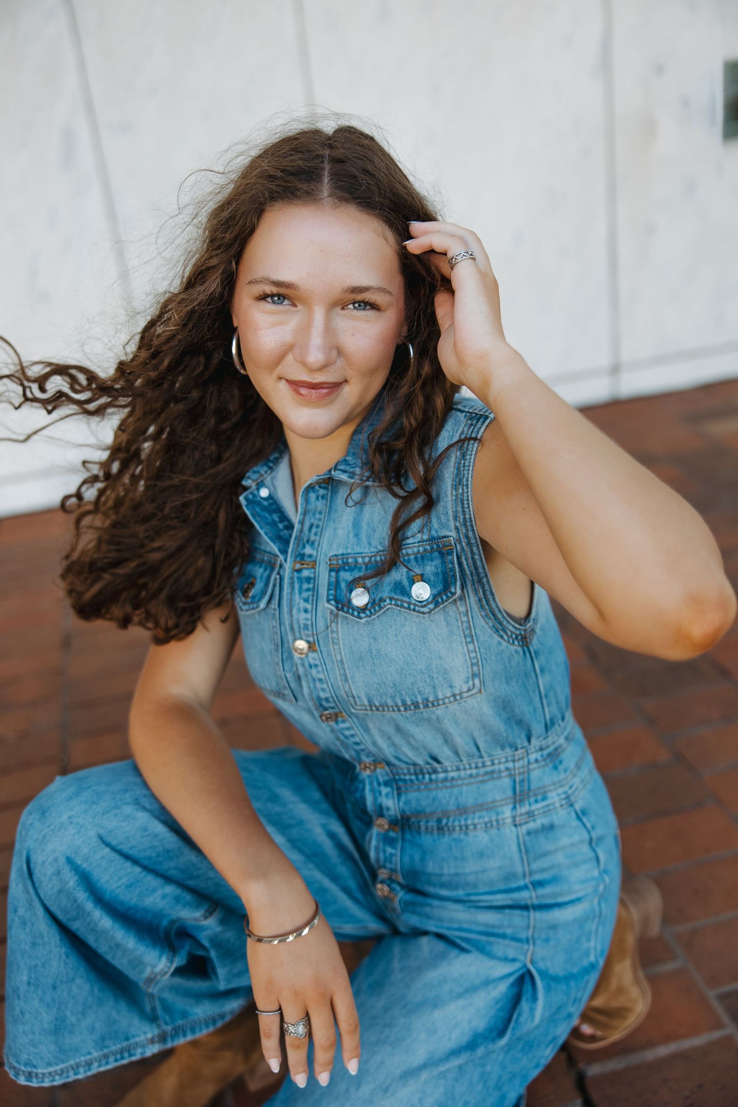 Person in denim overalls sitting on brick surface with white wall background.
