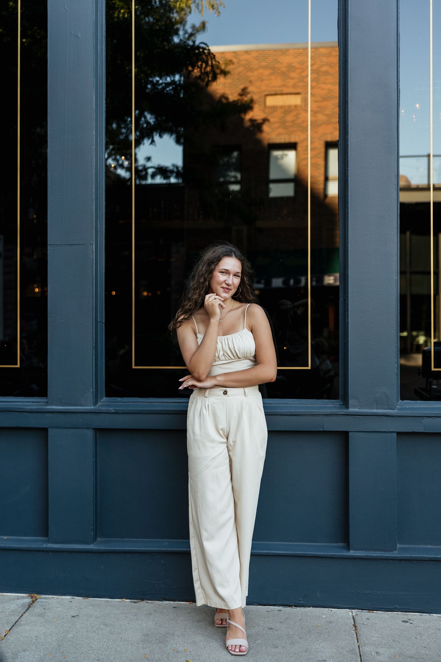 A person in a white outfit poses elegantly against a blue storefront window during golden hour.
