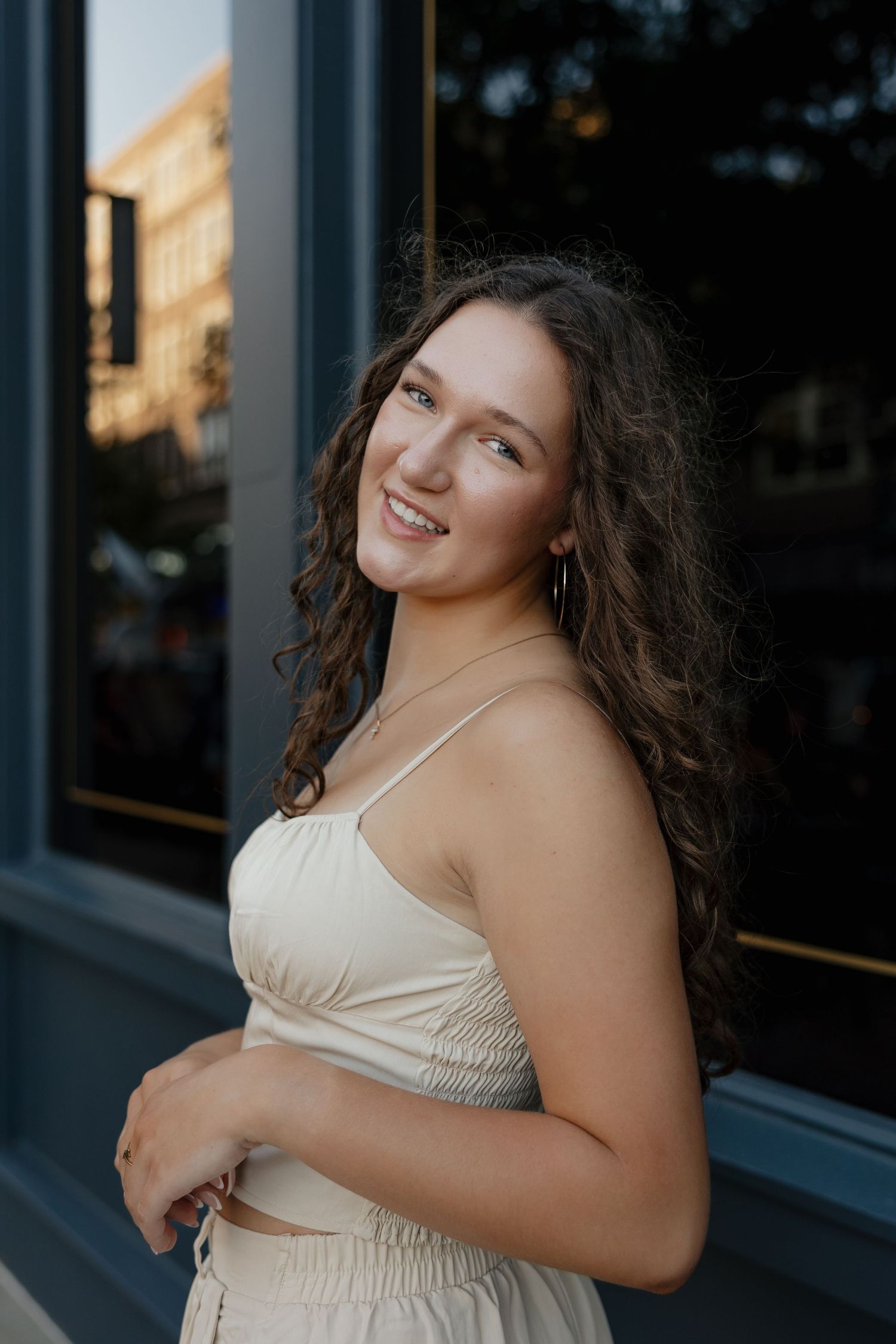 A portrait of someone wearing a cream-colored outfit smiling against a blue building exterior.