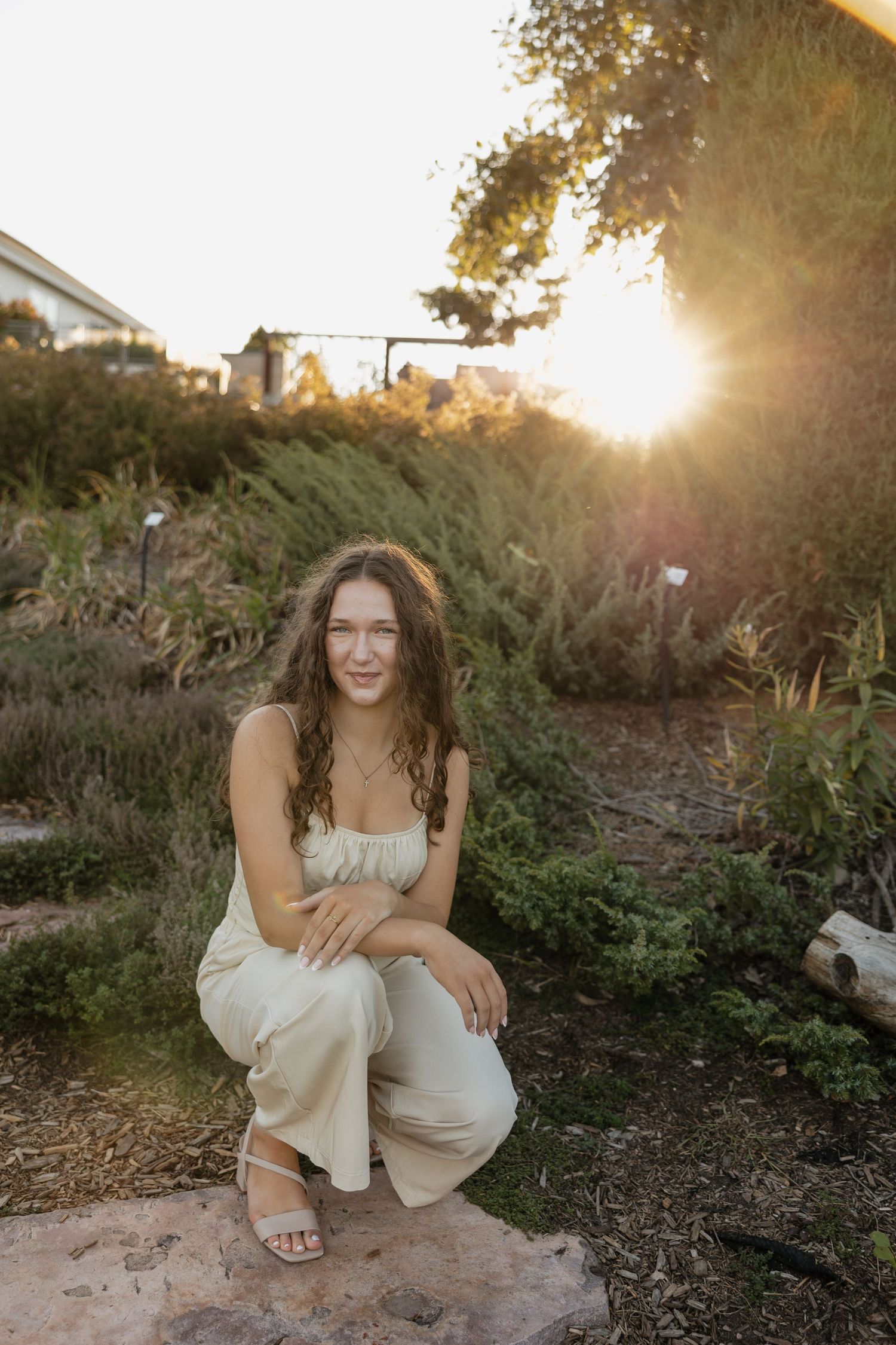 A sunset portrait of someone in white clothing crouching on rocks in a garden setting.
