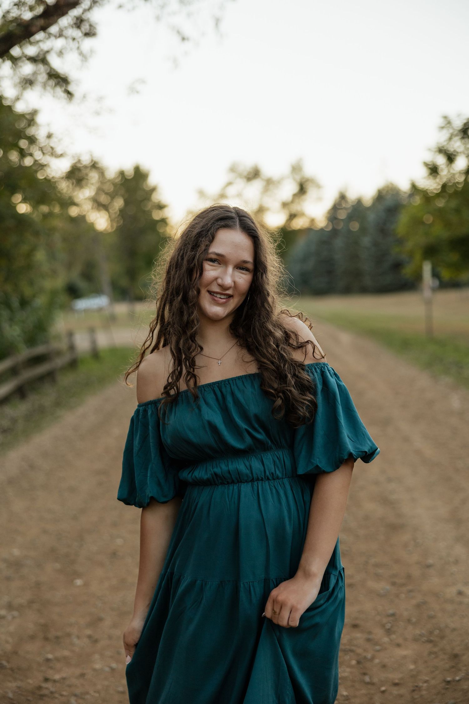 A candid shot of someone in a teal dress walking along a dirt path at sunset.