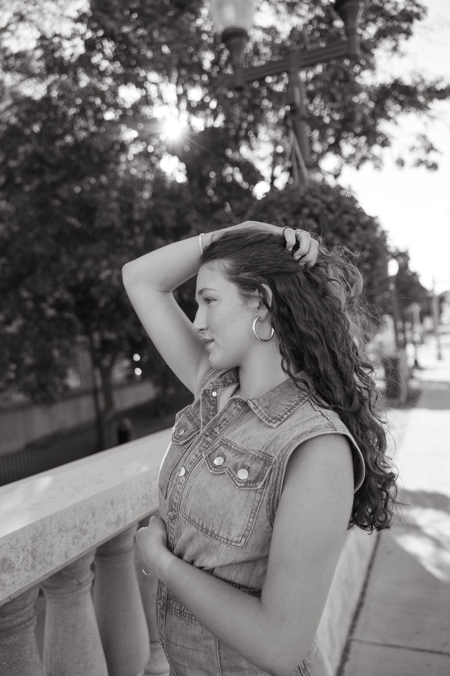 Black and white portrait of person in denim vest against urban backdrop with dramatic lighting.