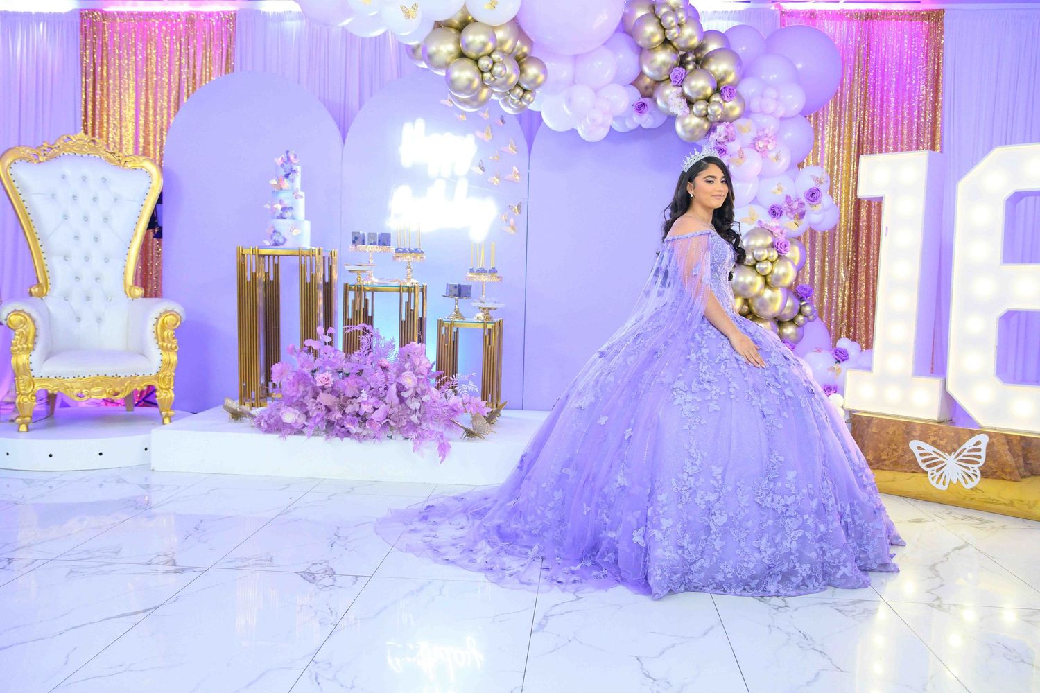 A lavender ballgown is showcased in an elegant room with purple lighting and balloon decorations.