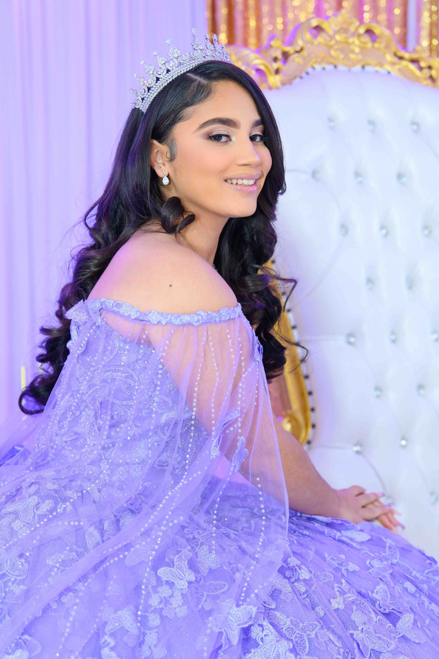 A lavender quinceañera gown with off-shoulder details and delicate embellishments glows in purple lighting.