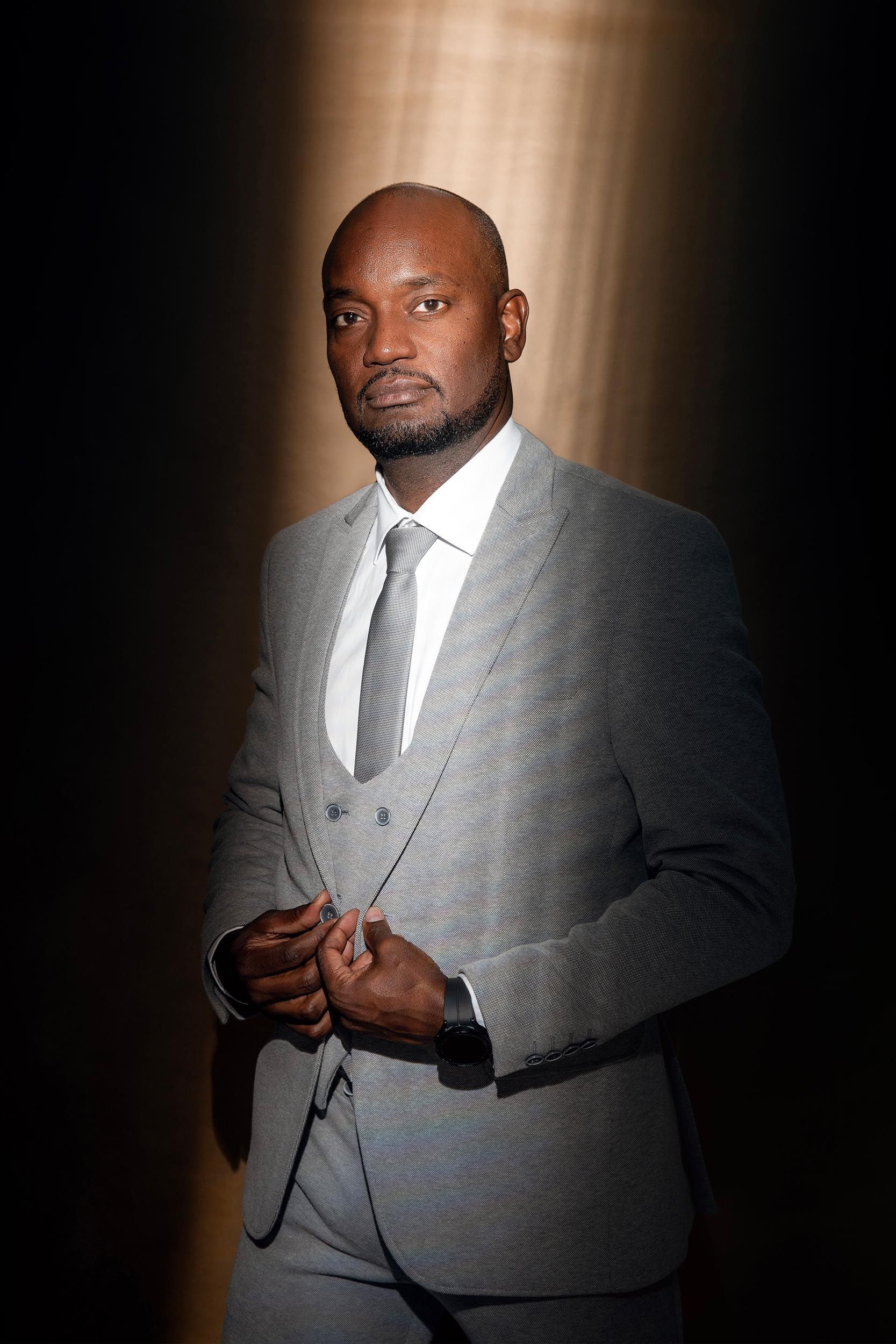 Dennis Martis, diputado of Bonaire, standing for a portrait in a grey suit with his hands  in Kralendijk in Felicia Schuette's photo studio.
