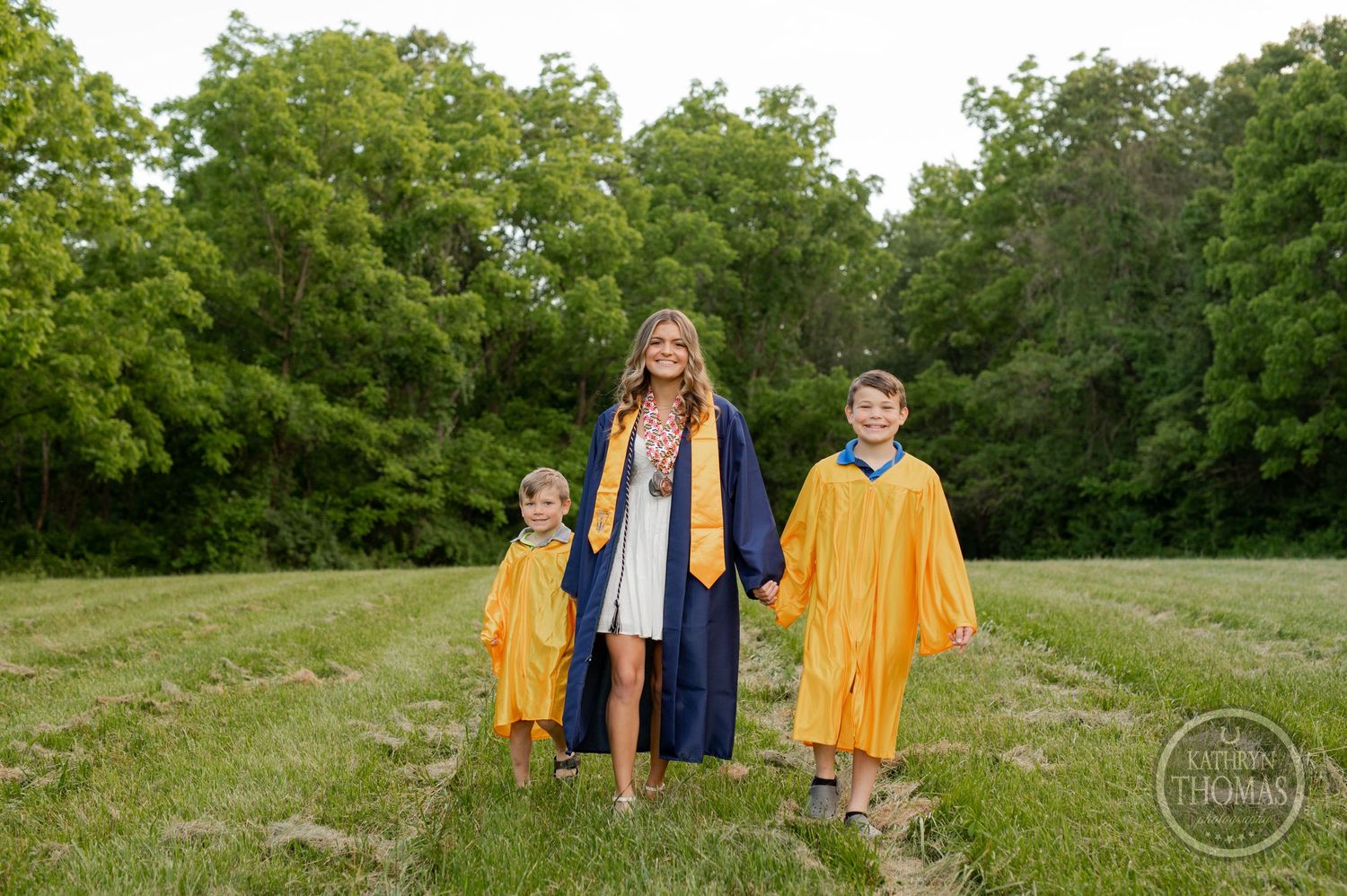 Graduates in yellow and blue regalia stand together on grassy path.