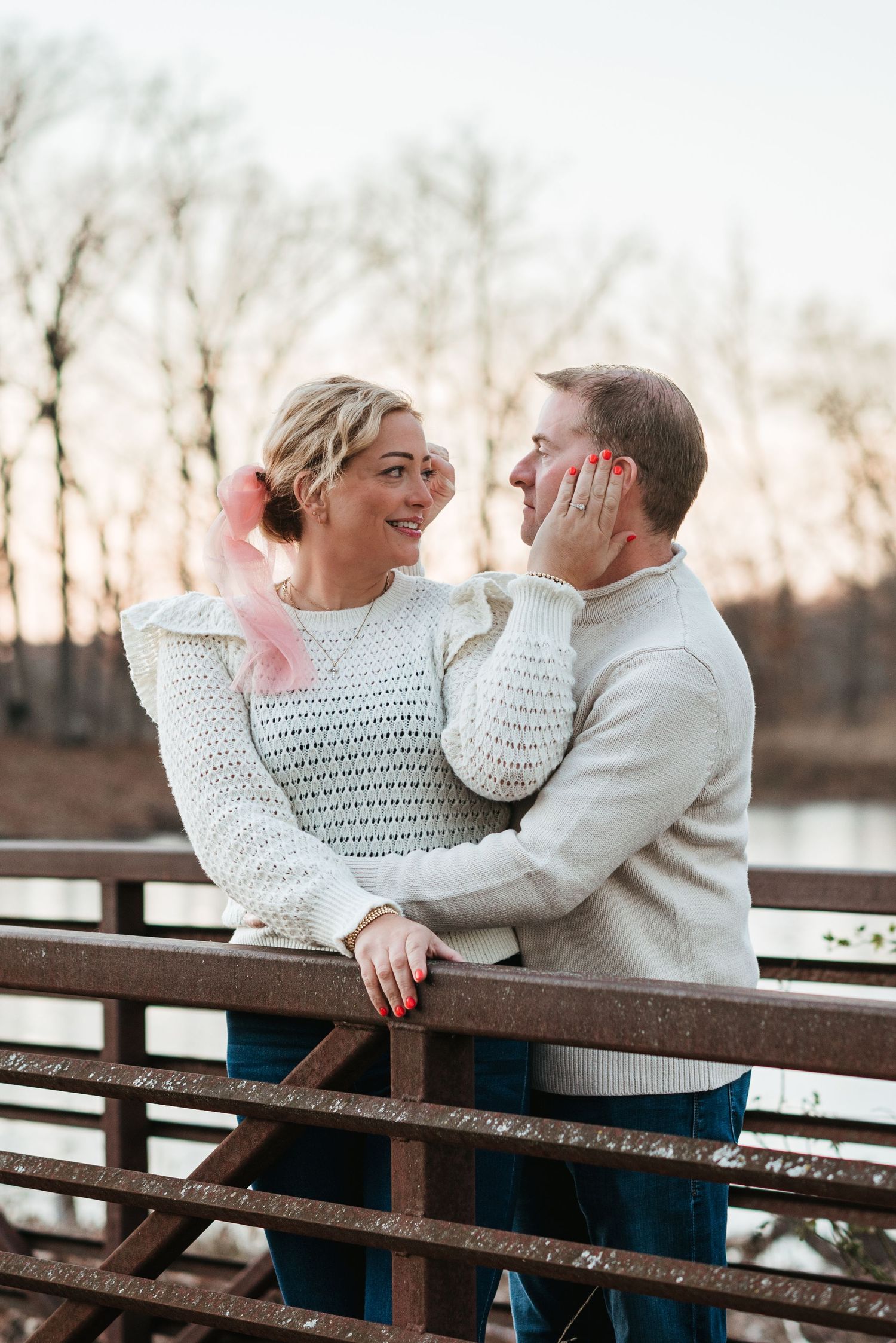 Couple in cozy sweaters sharing intimate moment on wooden bridge at sunset.