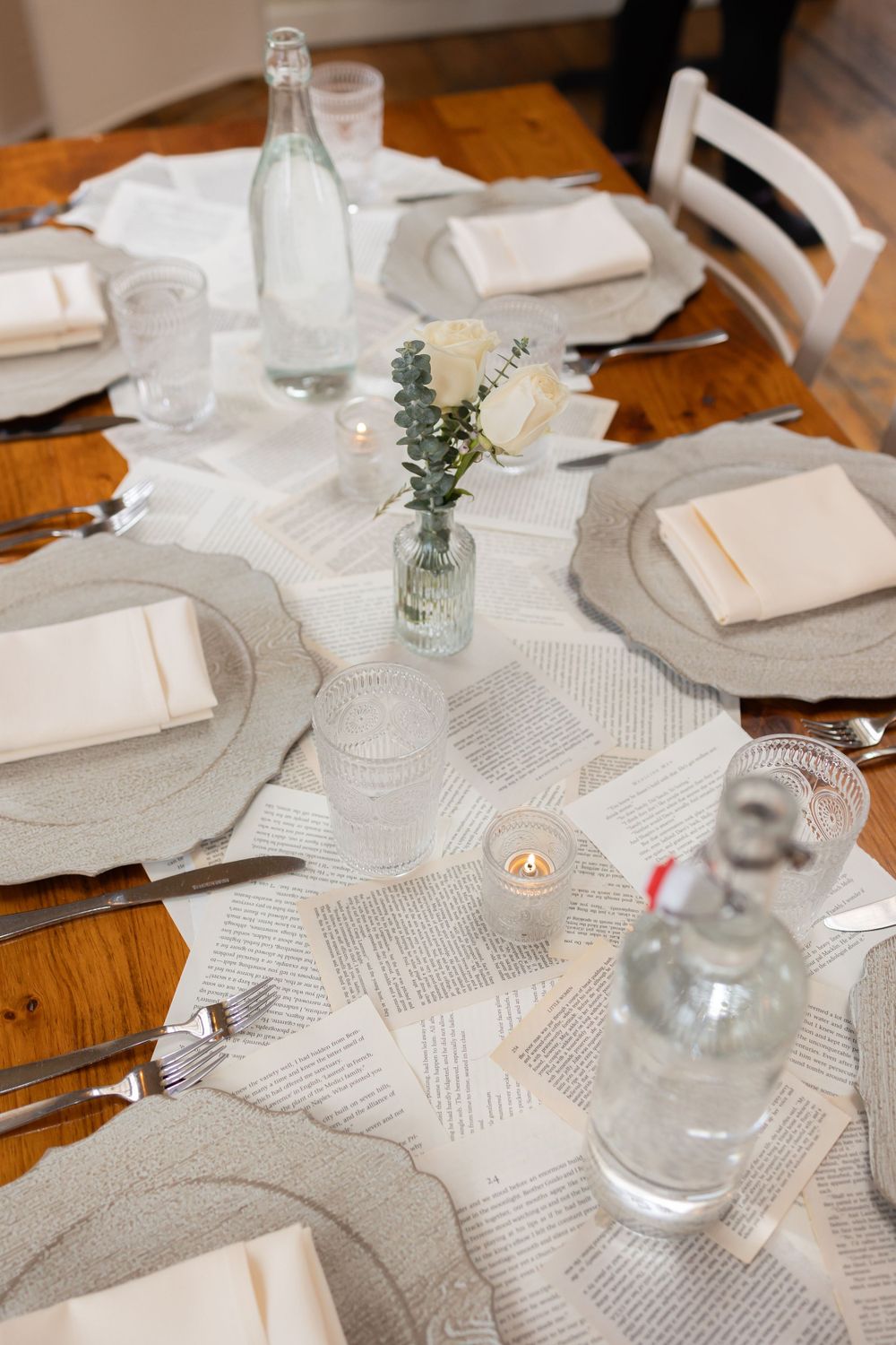 Elegant table setting with white linens, glass bottles and candles on wooden table.