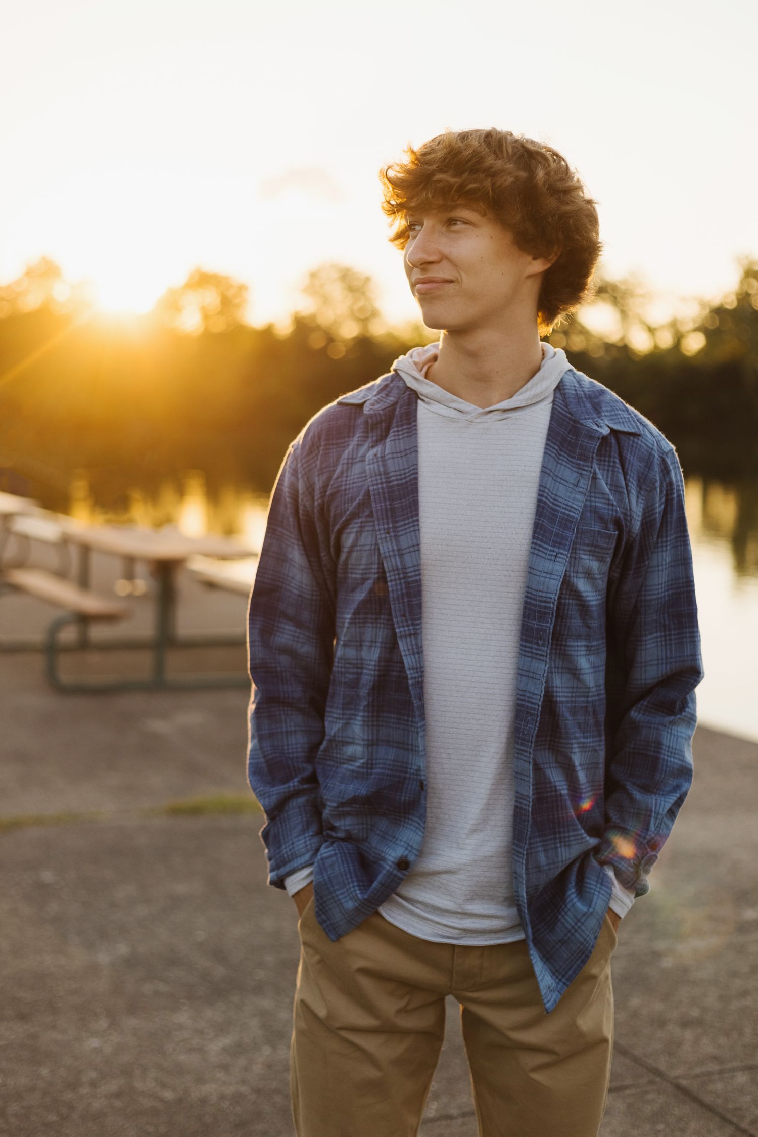 A golden hour portrait by the water featuring someone in layered casual wear.