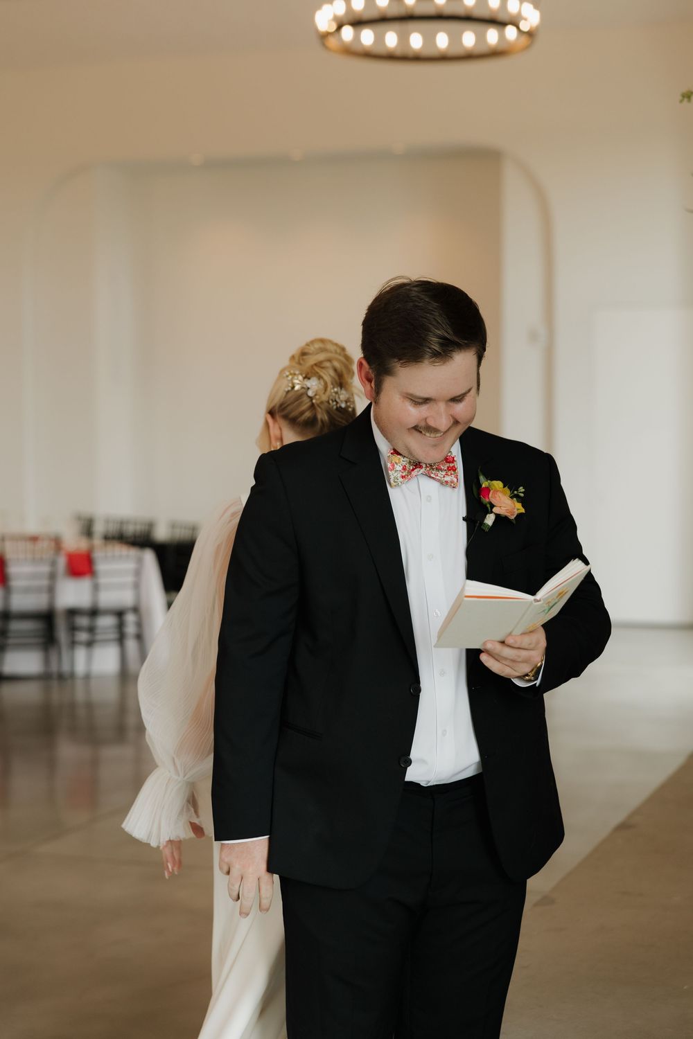 A couple in formal wedding attire shares a joyful moment together in an elegant venue with a chandelier overhead.