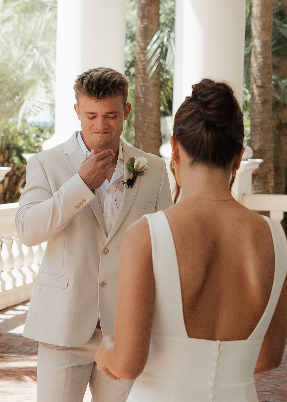 Emotional first look sequence between bride and groom in matching white attire under tropical palm trees.
