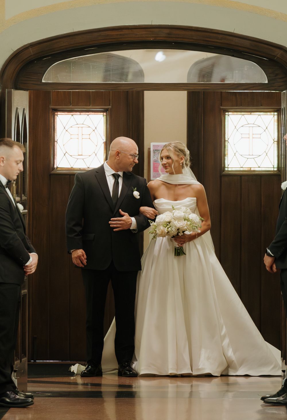 A romantic first dance sequence between newlyweds in a classic wood-paneled ballroom with stained glass windows.