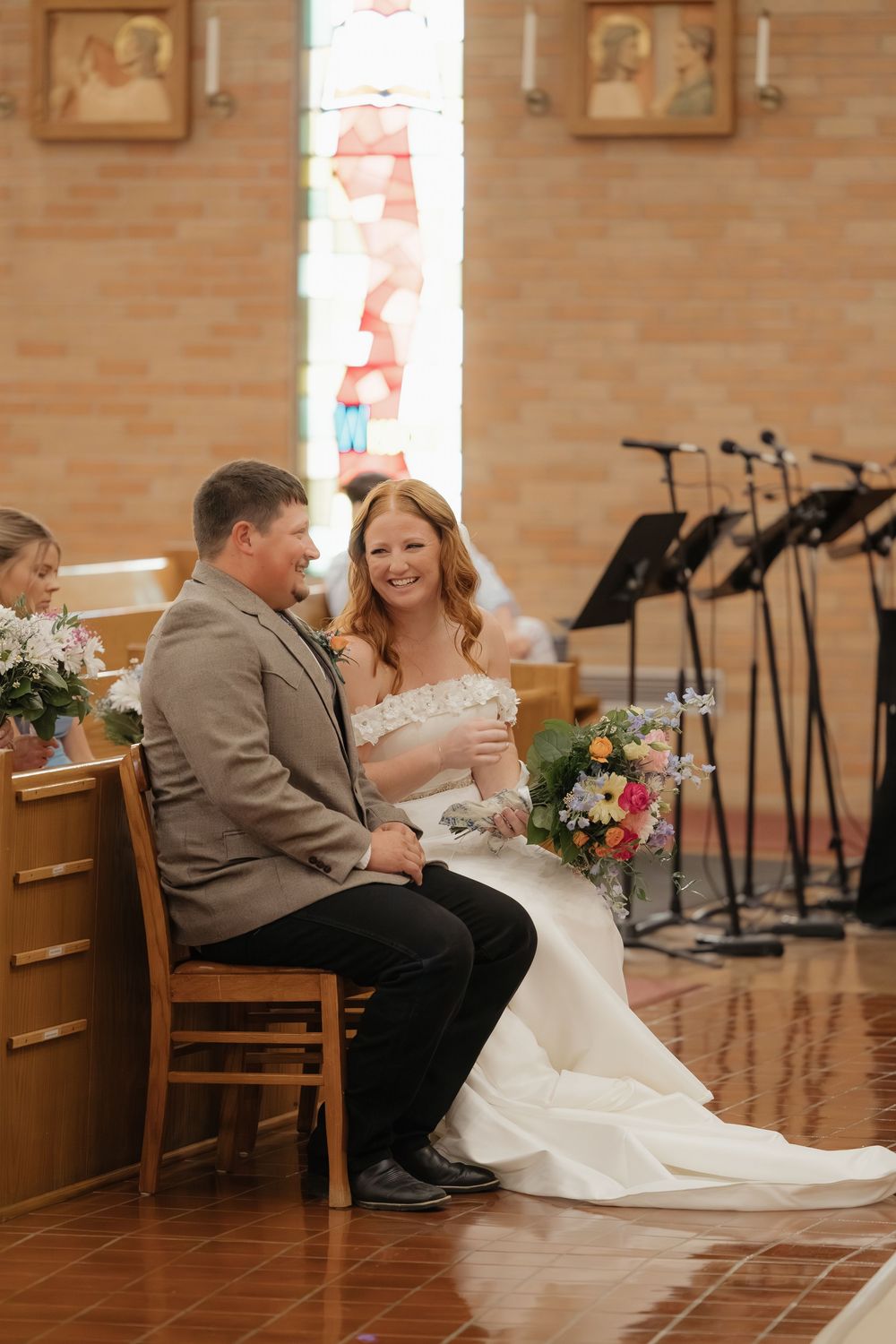 Bride and groom share an intimate moment sitting together at their wedding reception in a brick-walled venue.