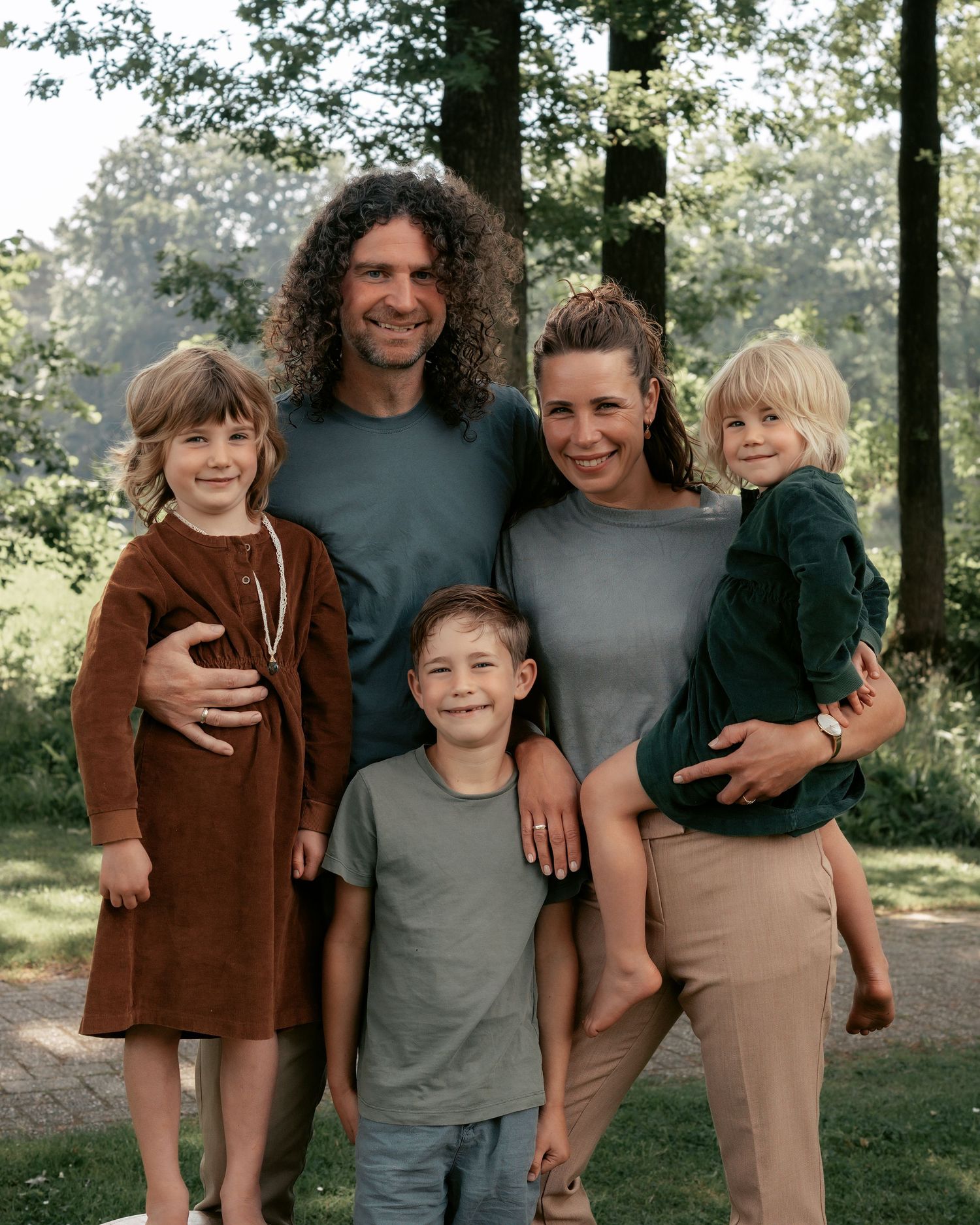 Group portrait of family members standing together in a wooded outdoor setting.