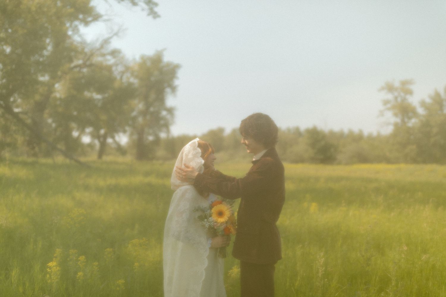 Ethereal sunlit wedding portrait in a golden field with soft focus effect.