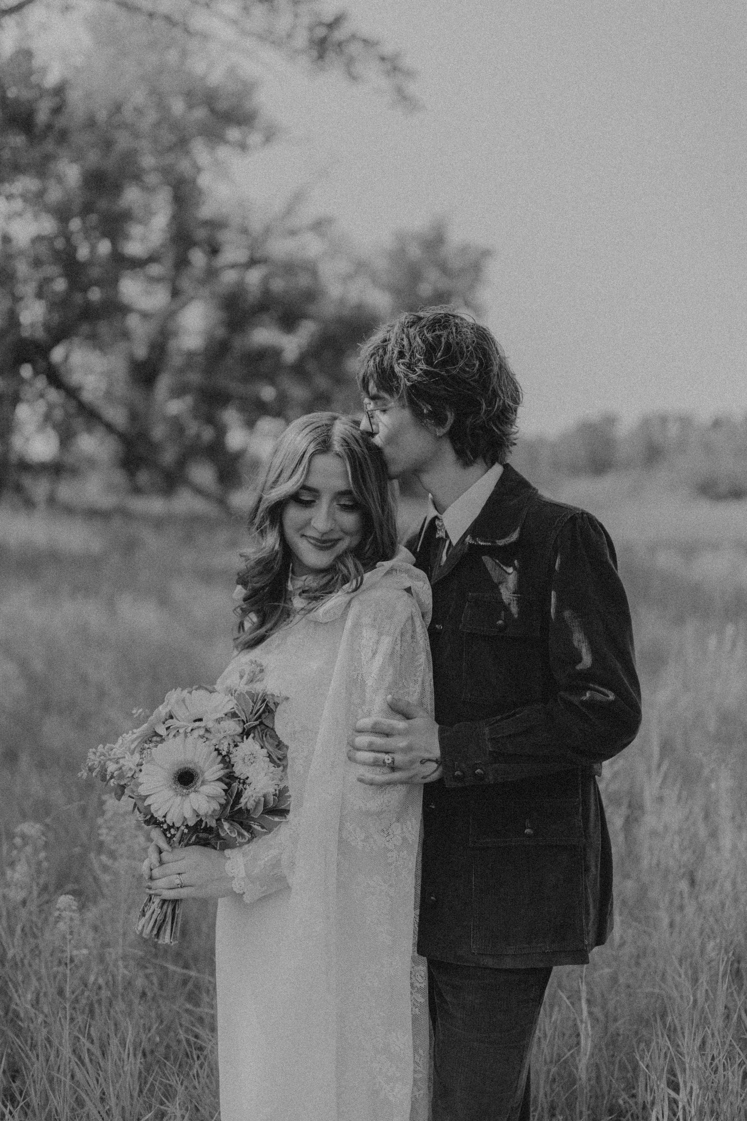 Black and white portrait of newlyweds embracing in tall grass field.