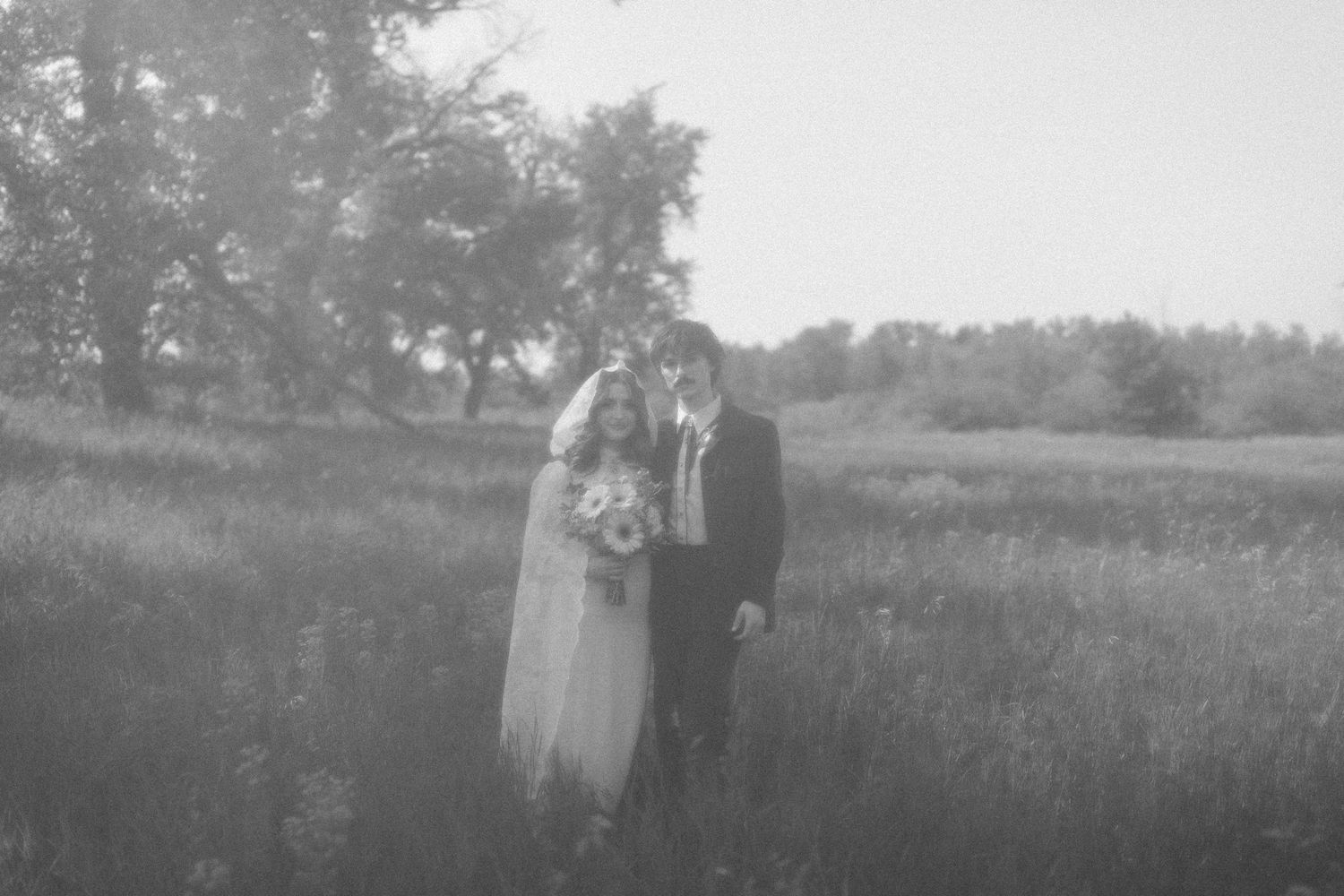 Dreamy black and white wedding portrait in a misty field with tall grass.