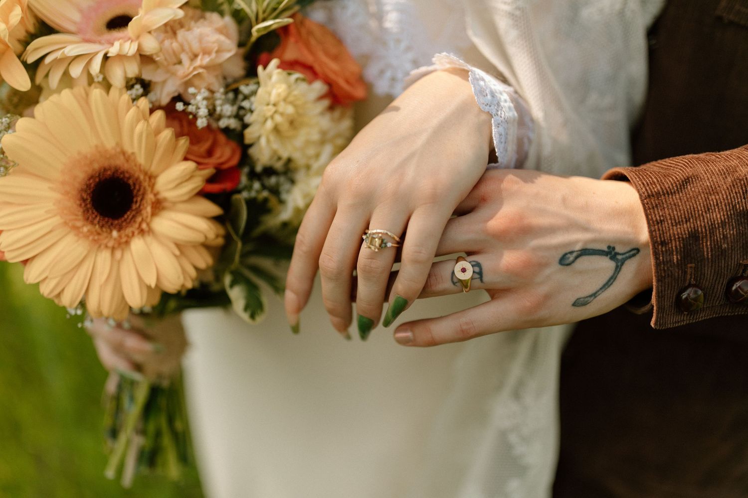 Close-up of hands holding bouquet with gerbera daisies and visible tattoos.