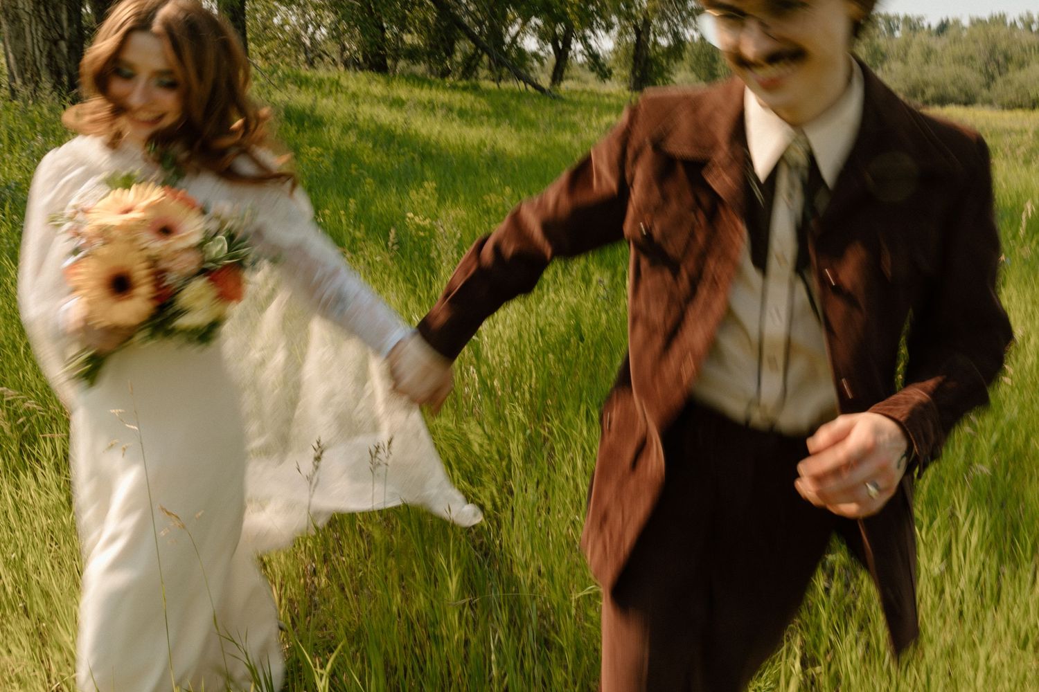Couple in vintage attire poses playfully in a grassy meadow at golden hour.