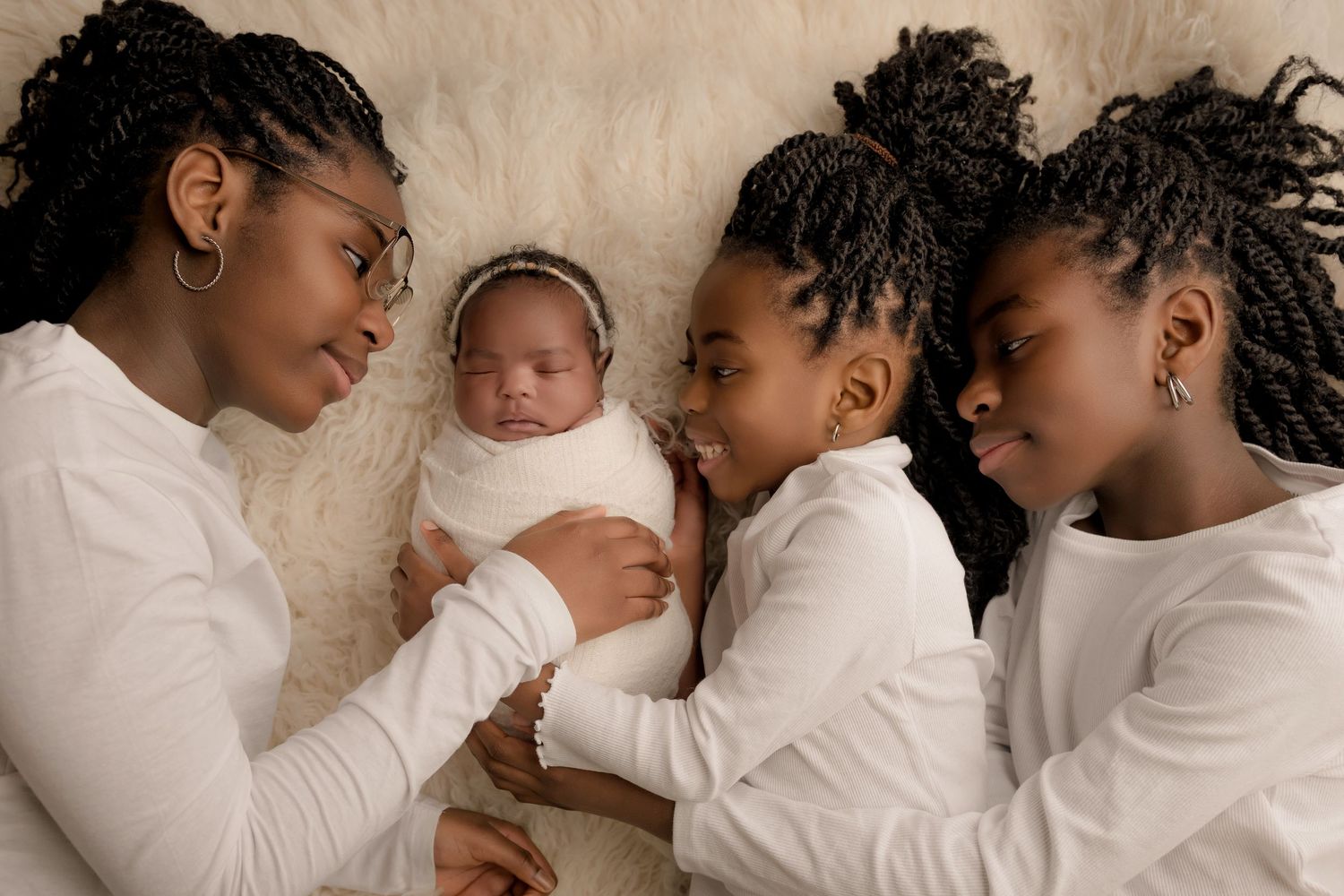 Newborn and Siblings in neutral clothing snuggle together on a soft cream-colored blanket during a newborn and family photo session.