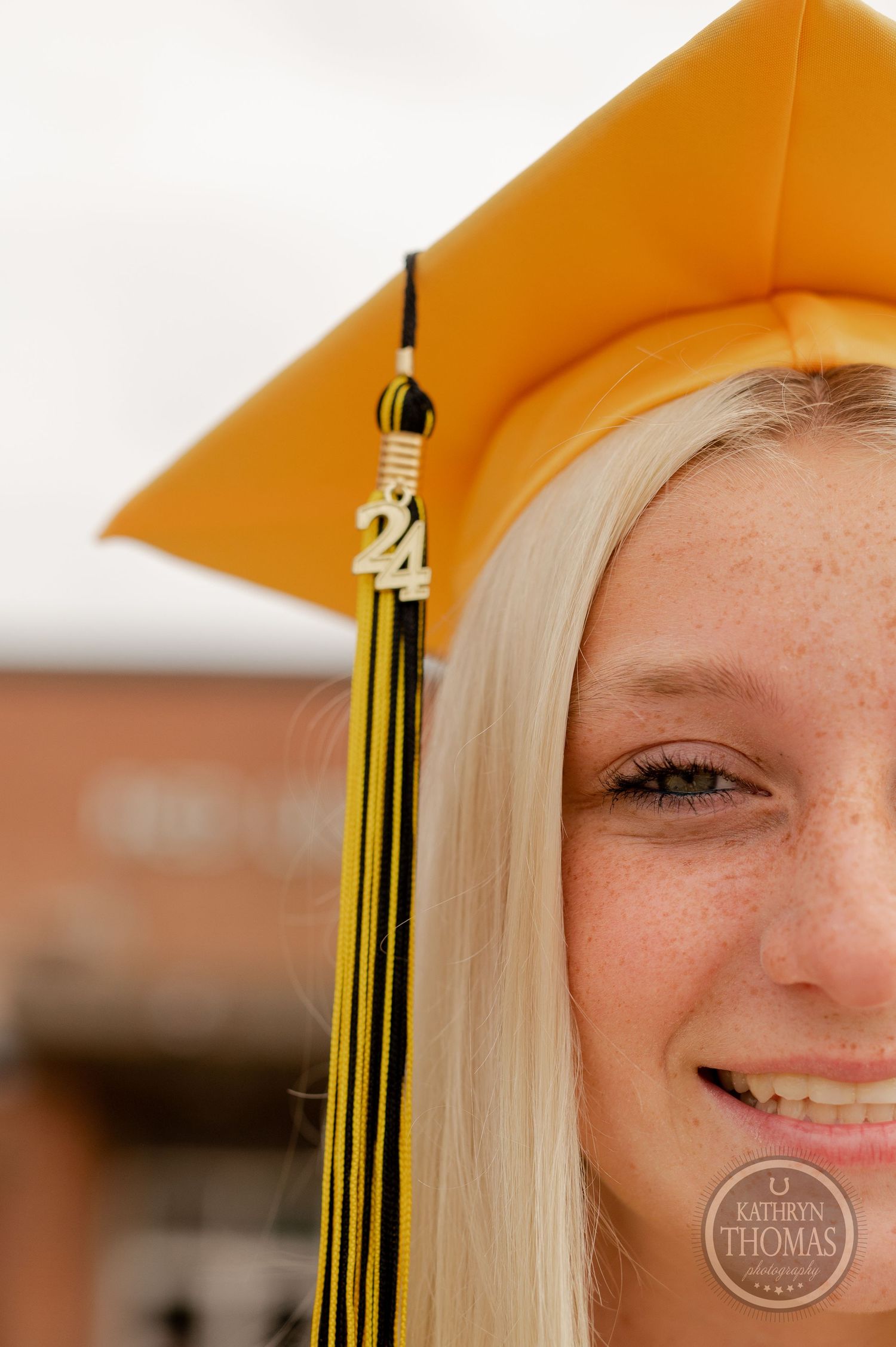 Close-up of gold graduation cap with tassel against brick building background.