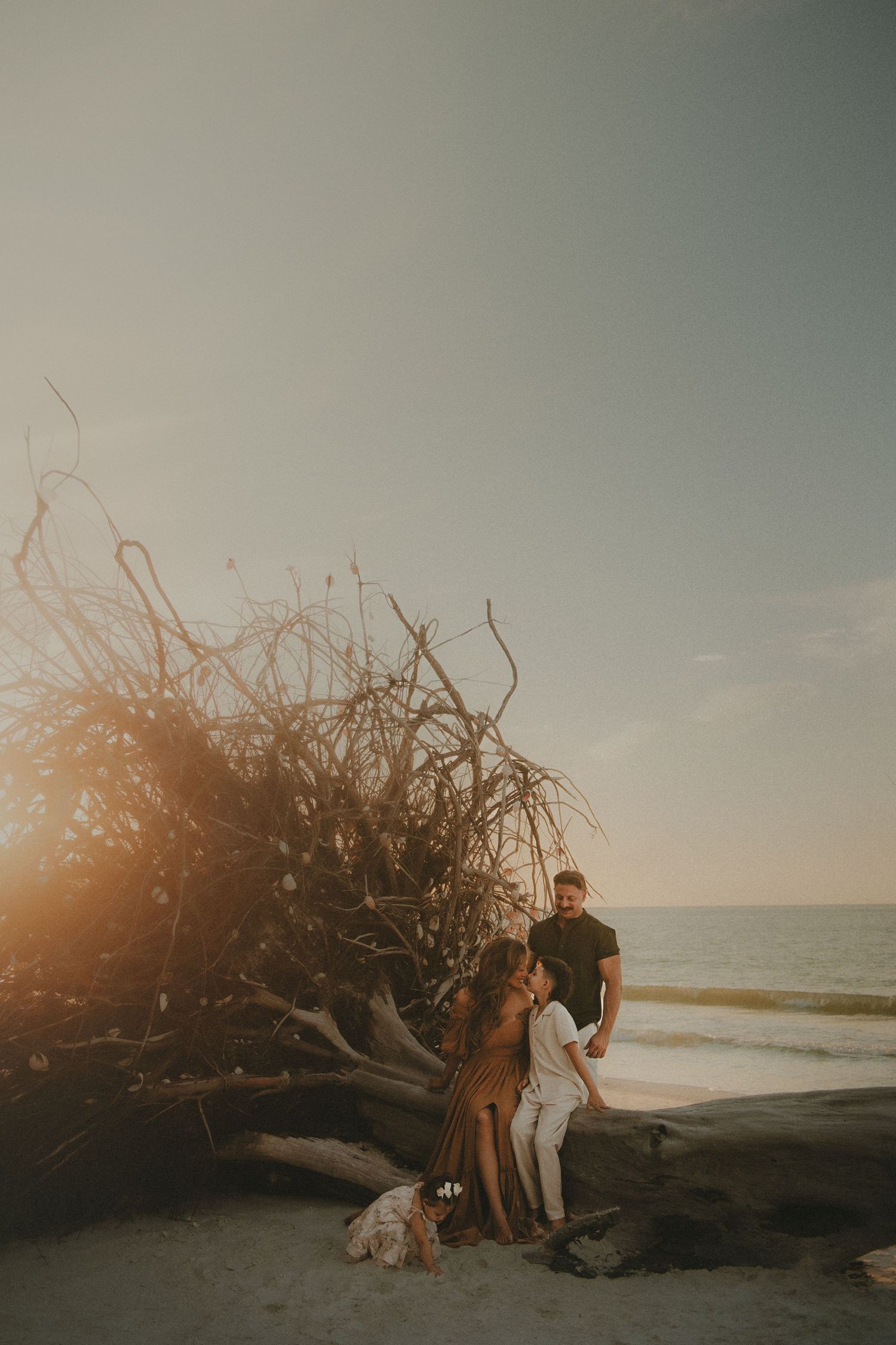 Couple embracing on rocky shore during dramatic golden sunset over ocean waves.