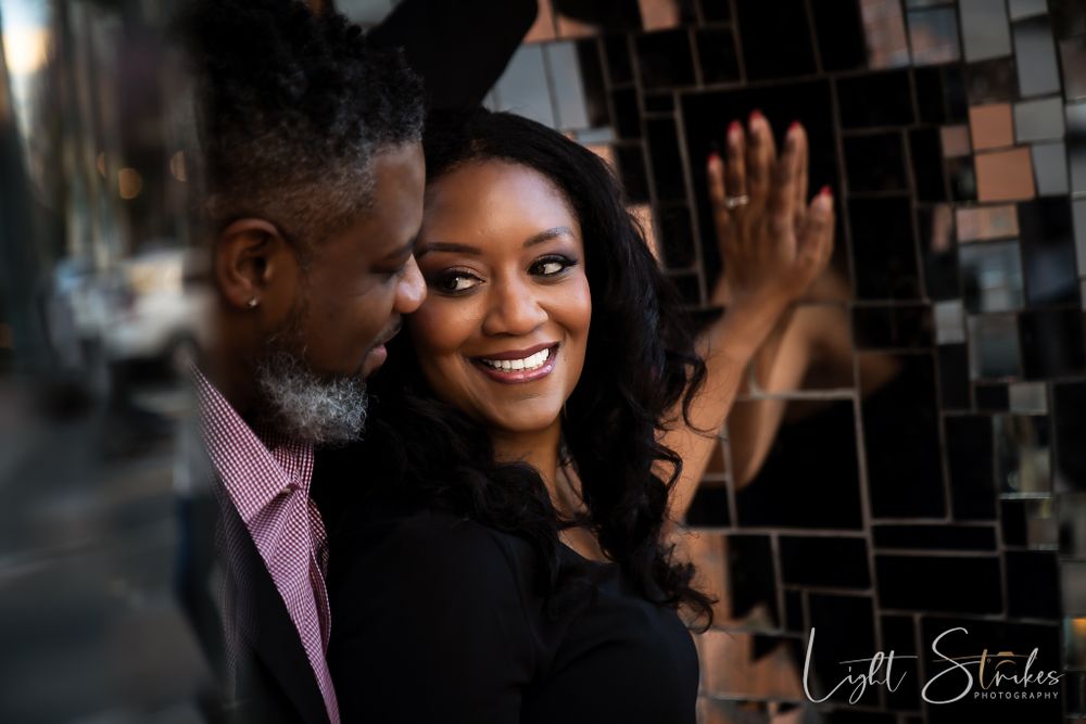 A couple shares an intimate moment together while smiling against a dark tiled wall captured by wedding photographer in Charlotte..