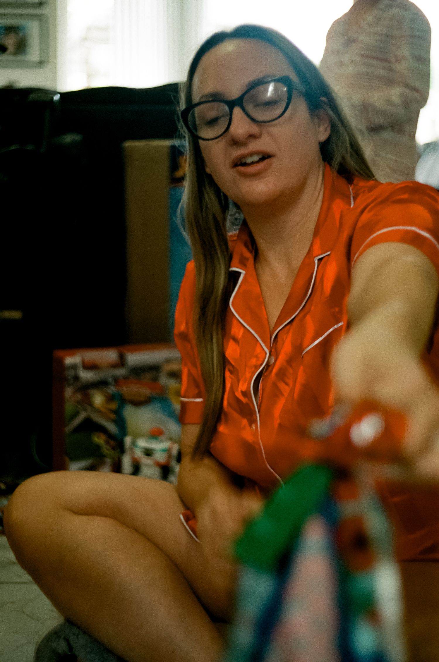 Person in orange pajamas sitting on floor during holiday celebrations.