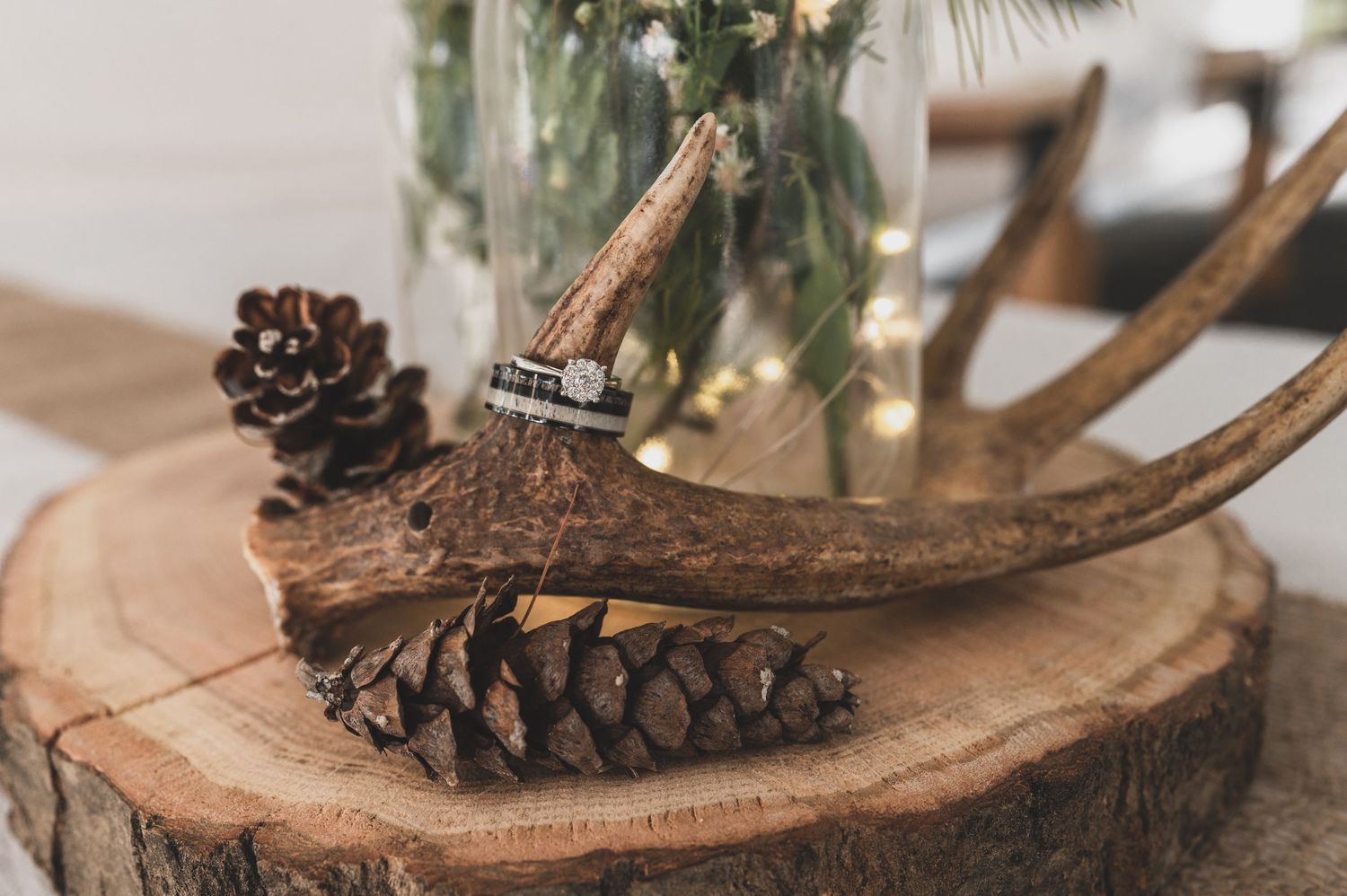 Rustic wedding decor featuring pine cones and antlers on a wood slice with greenery.