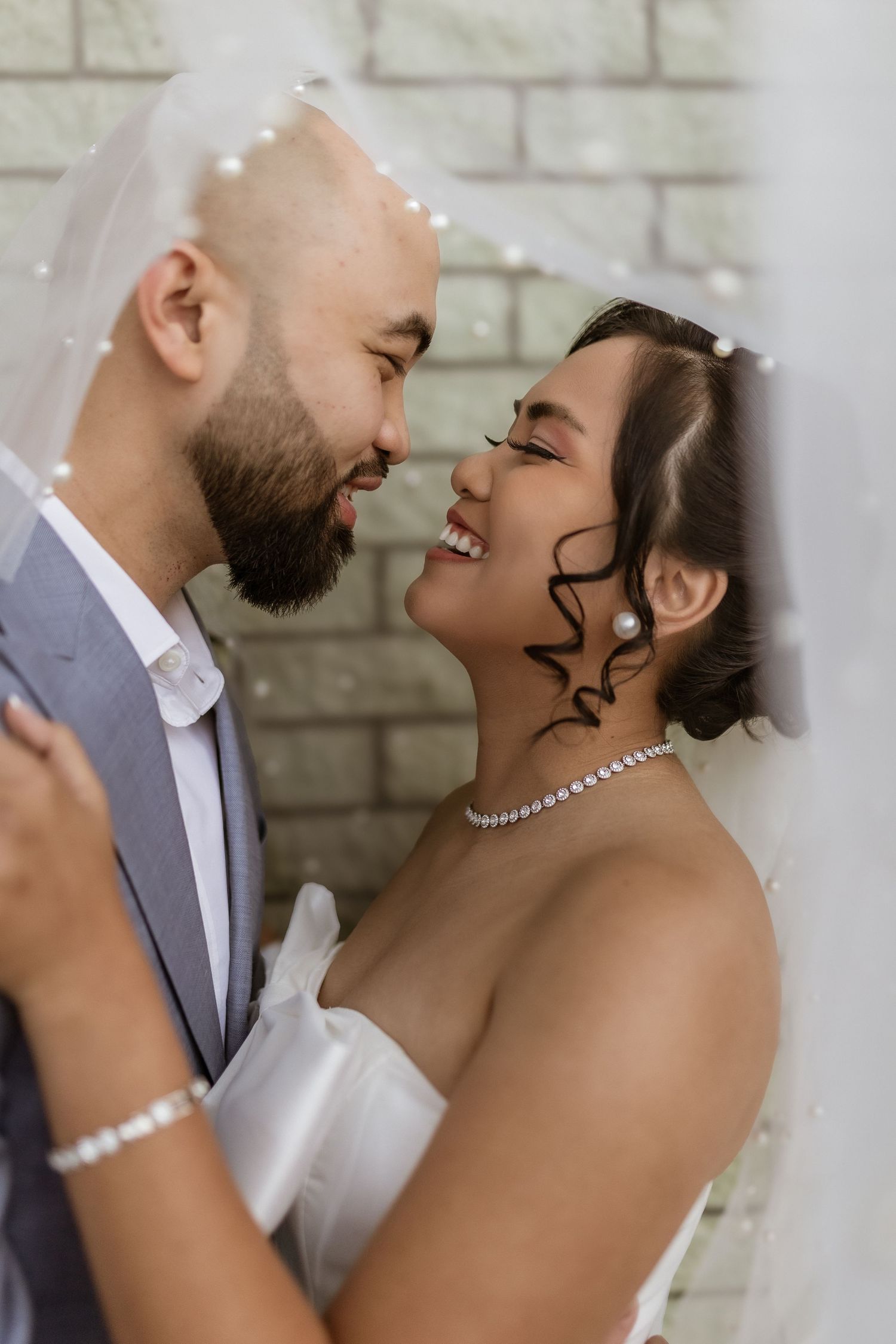 An intimate wedding portrait of a couple sharing a loving moment against a white brick wall.