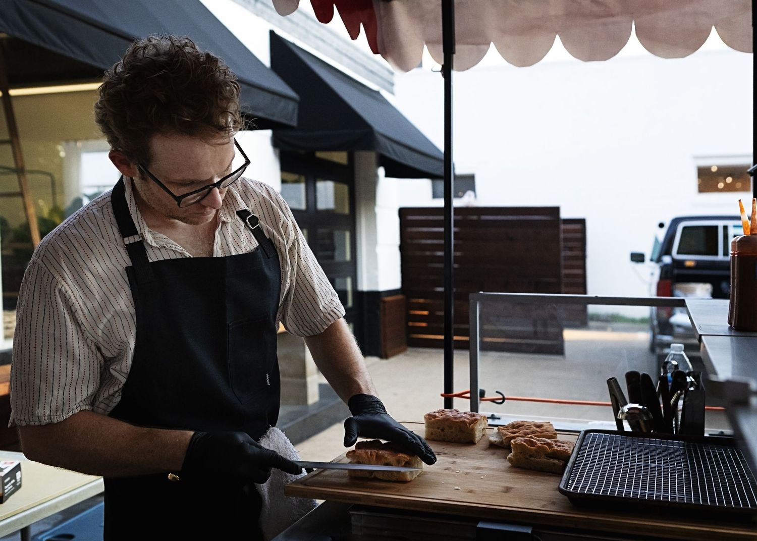 Worker in apron and gloves preparing food at outdoor market stall.