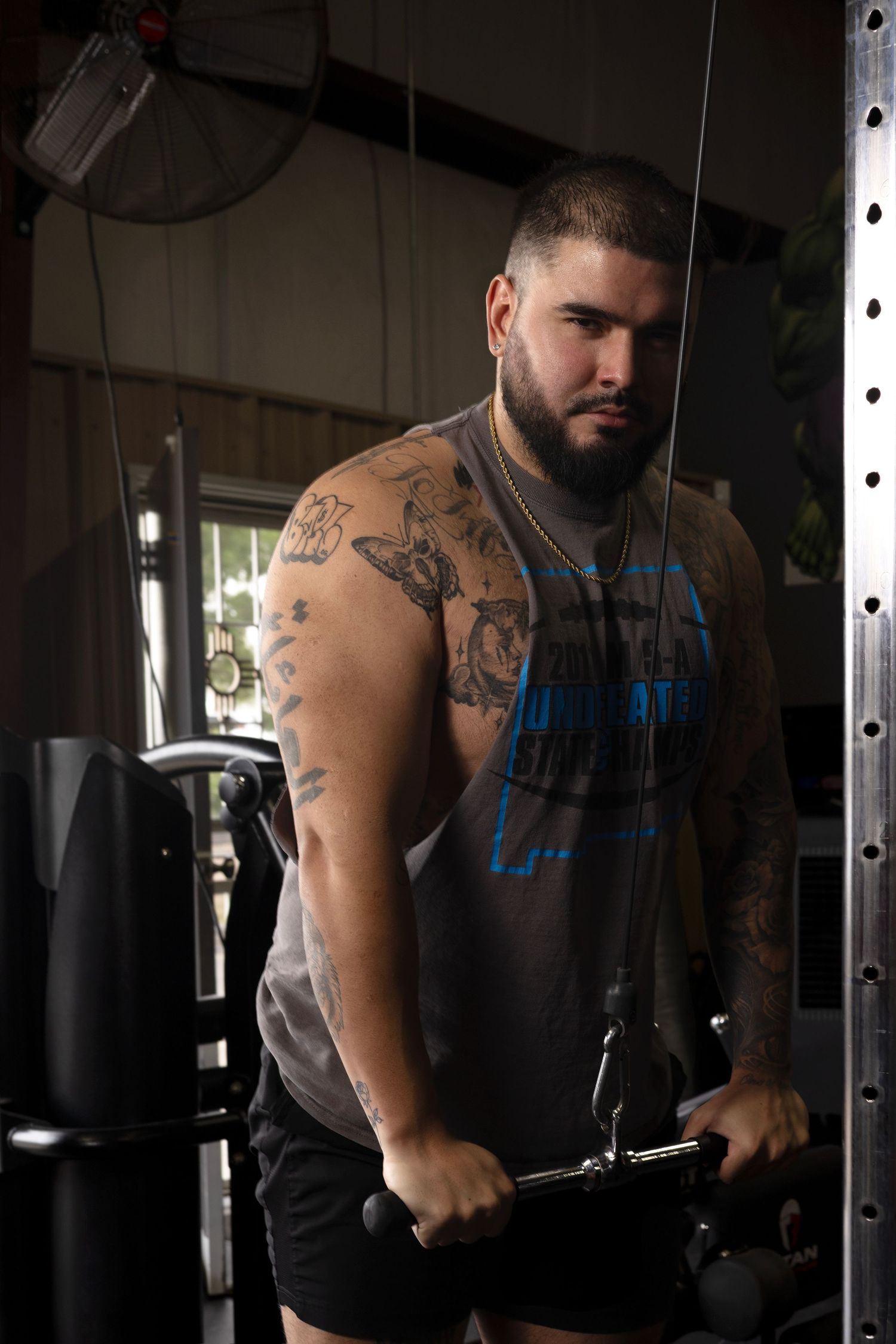 Muscular athlete performing cable exercise in dark gym setting.