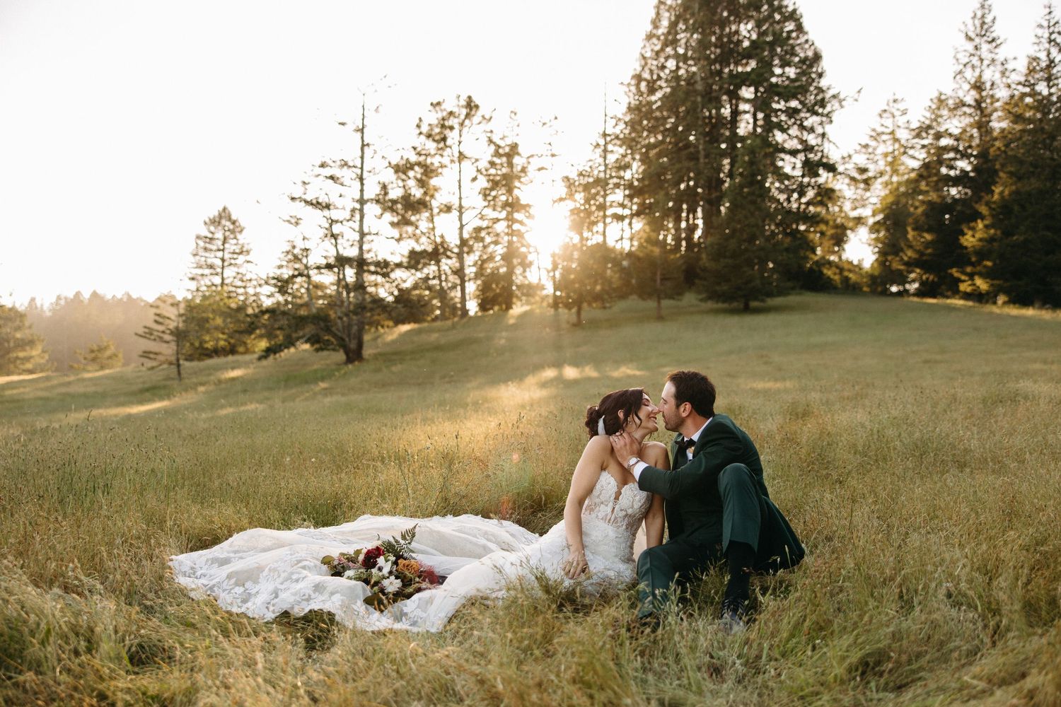 Romantic couple embraces in front of rustic barn wall with yellow wildflowers in foreground.