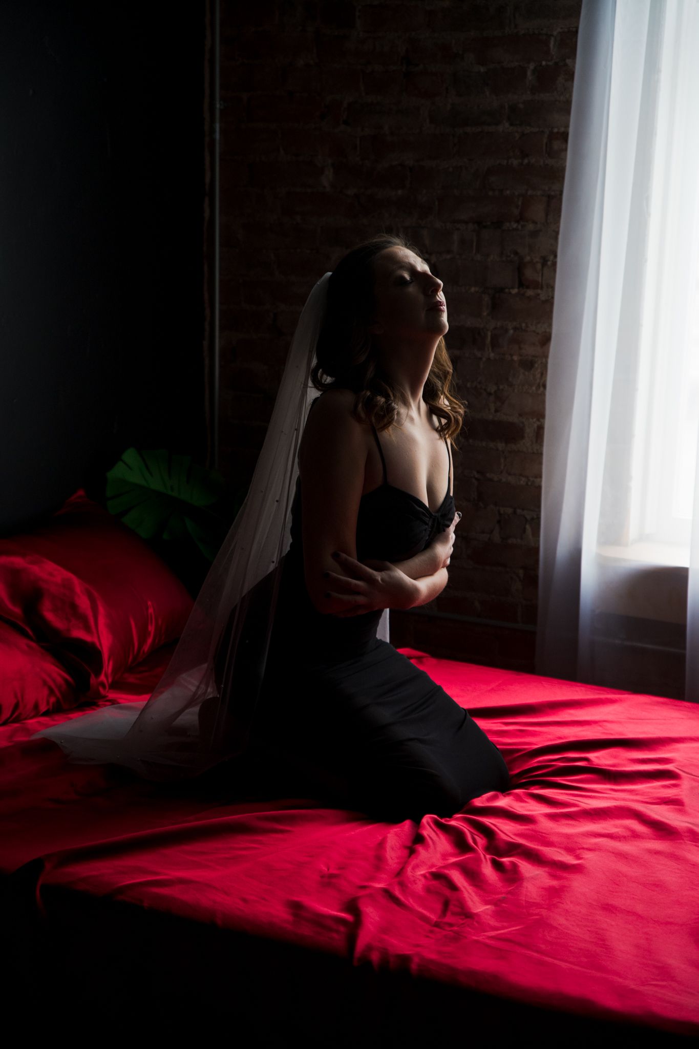 Dramatic bridal boudoir photo with silhouette against window and red bedding.