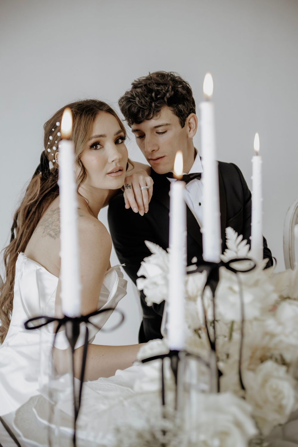 Bride and Groom pose together surrounded by candles. Groom is looking at the bride