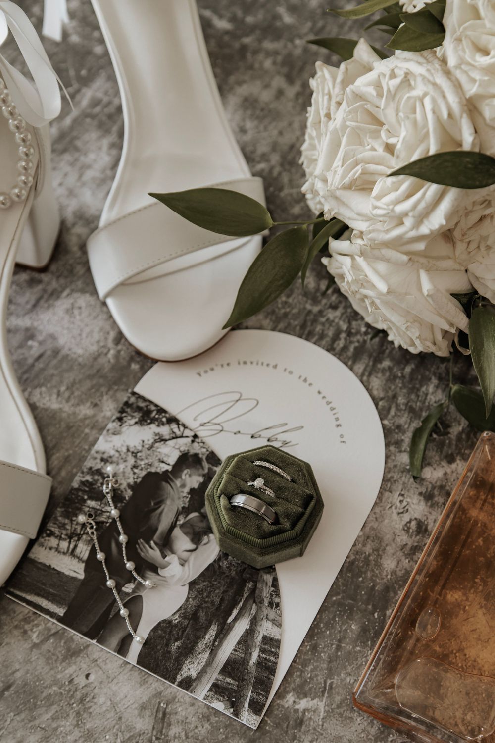 Detail photo of brides shoes, wedding invitation, flowers, and wedding rings