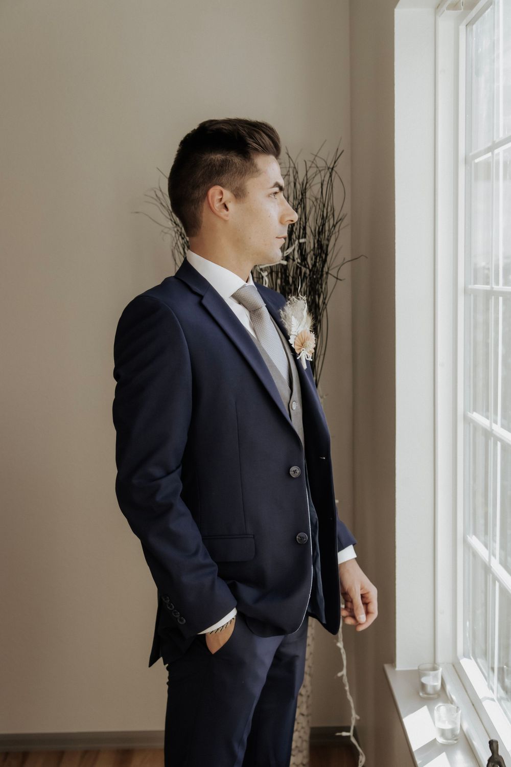 Groom in tux looks out the window before ceremony