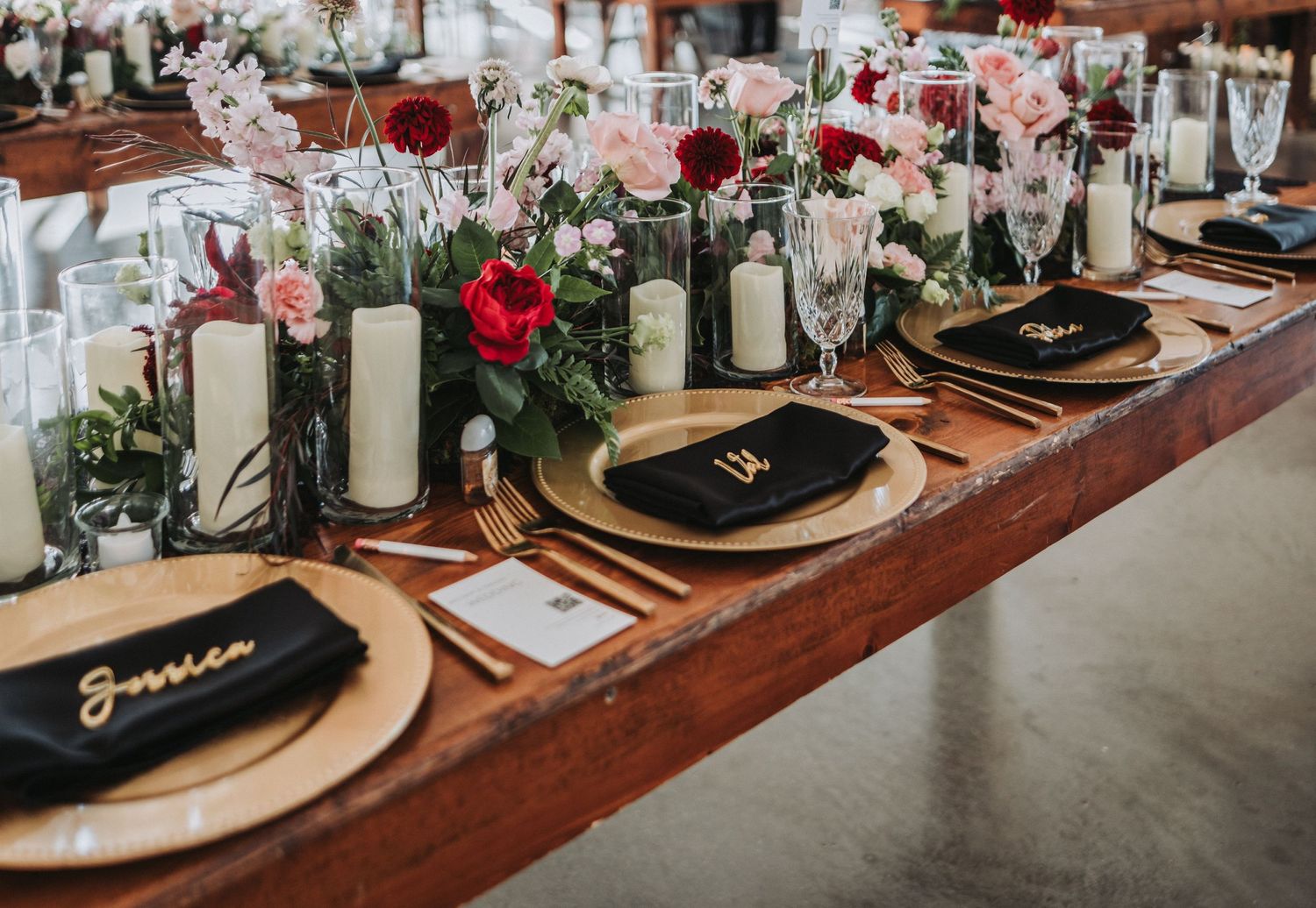Wedding table decorated with gold chargers, candles, and red and pink floral arrangements.