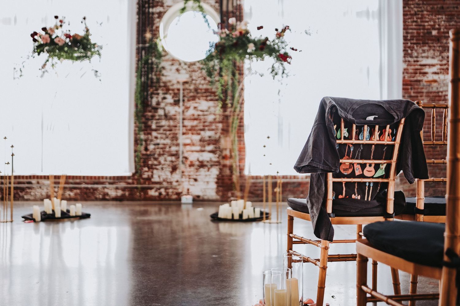 Industrial wedding ceremony space with exposed brick wall and floral arch decorations.